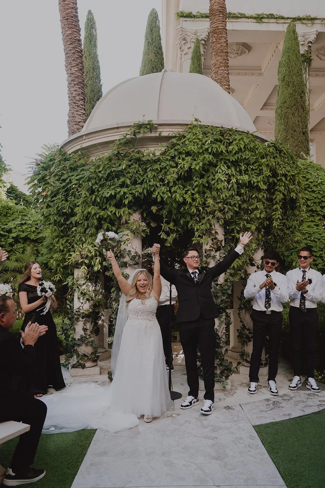 Bride and groom raising their arms in the air in celebhration as they walk back down the aisle as husband and wife after their Caesars Palace Venus Garden wedding ceremony
