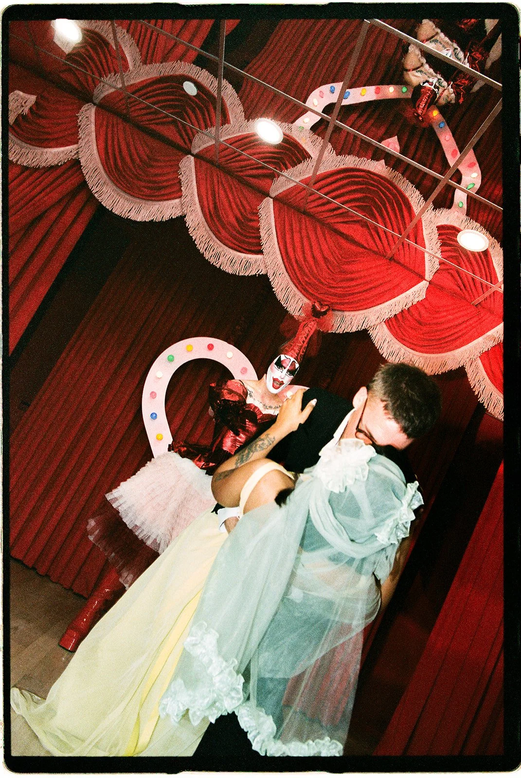 Newlyweds kissing in front of red velvet curtains and a pink heart-shaped arch at Sure Thing NYC.