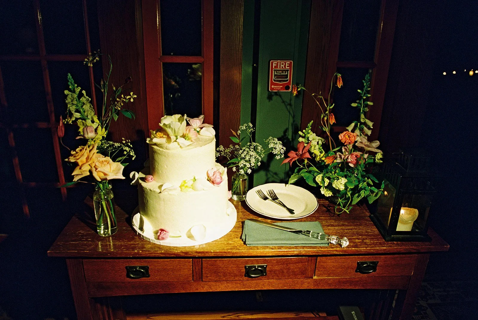 Film wedding detail photo of a two-tier cake decorated with flowers and surrounded by colorful floral arrangements.