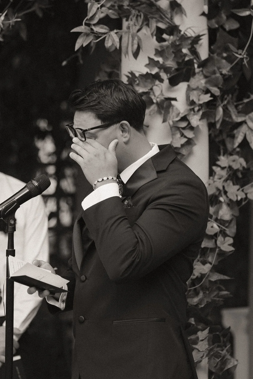 Close up black and white photo of the groom getting emotional as he reads his vows