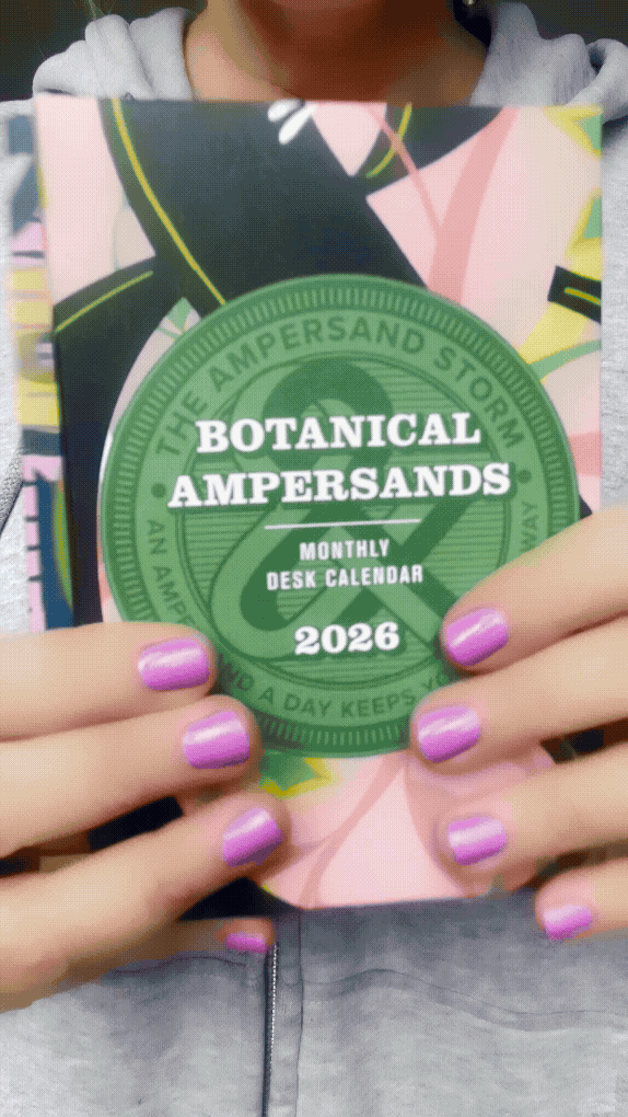 Closeup of hands displaying two brightly colored illustrated ampersand calendars