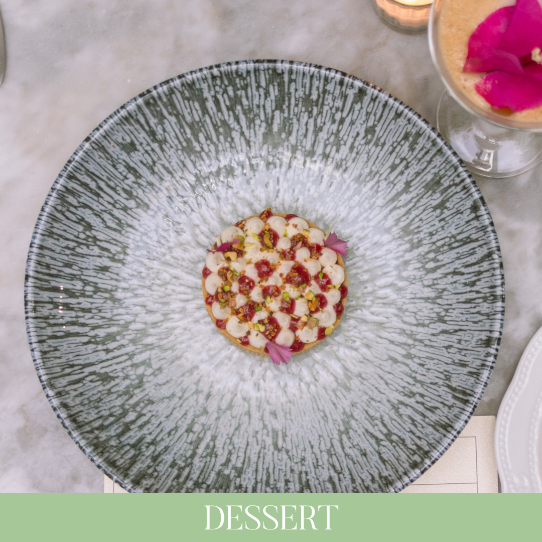 Postre decorado con pistachos, pétalos de rosa y pequeñas gotas de salsa de fresa en un plato