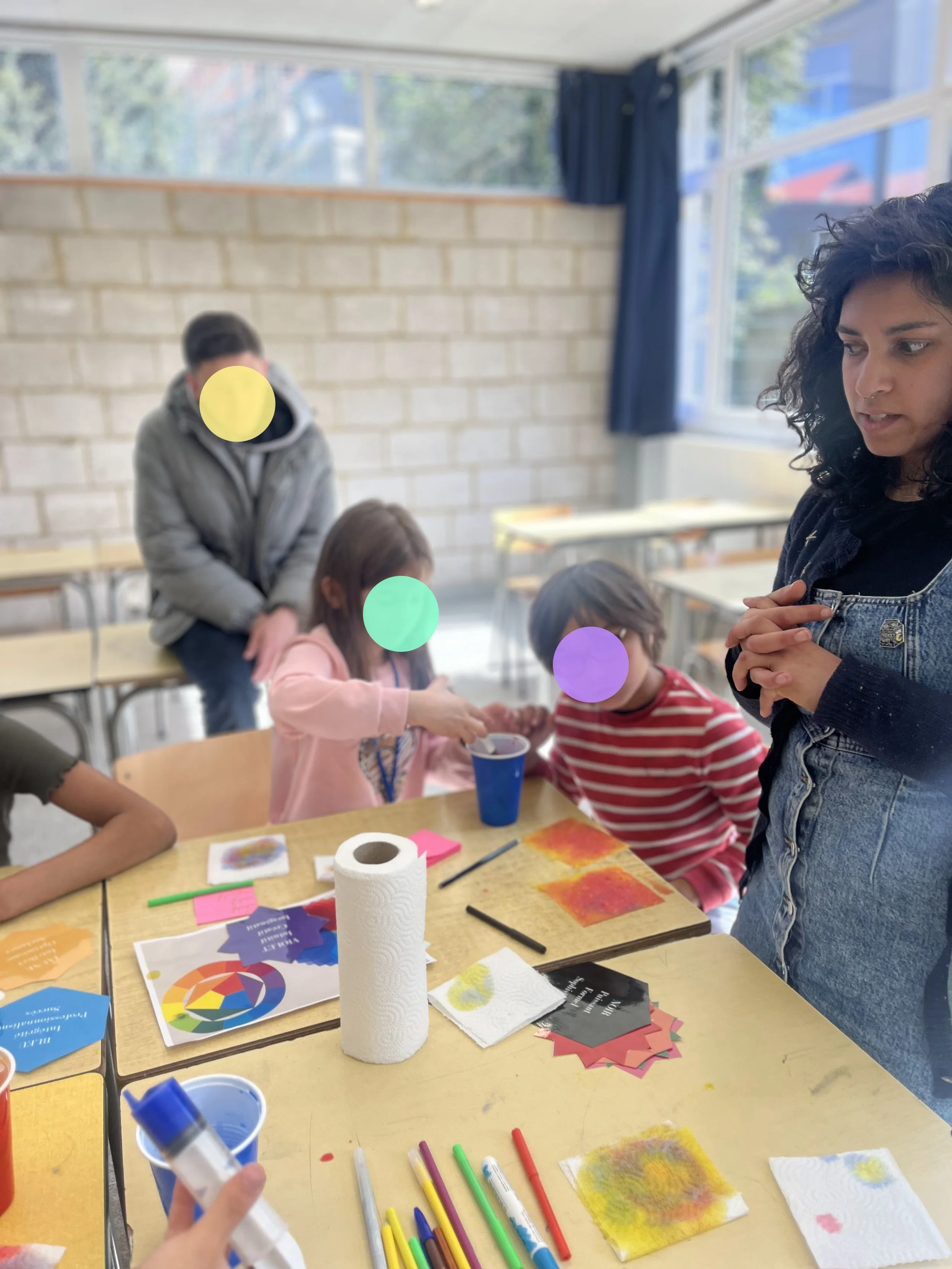 Une classe d'enfants en train de faire des activités artistiques avec des adultes, autour d'une table avec des fournitures de peinture et des papiers colorés.