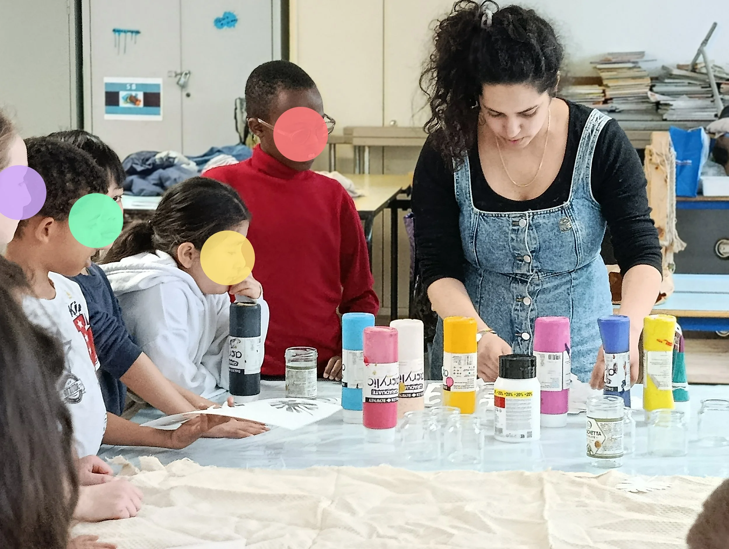 Un groupe d'enfants et une adolescente participent à une activité artistique avec des pots de peinture multicolores sur une table.