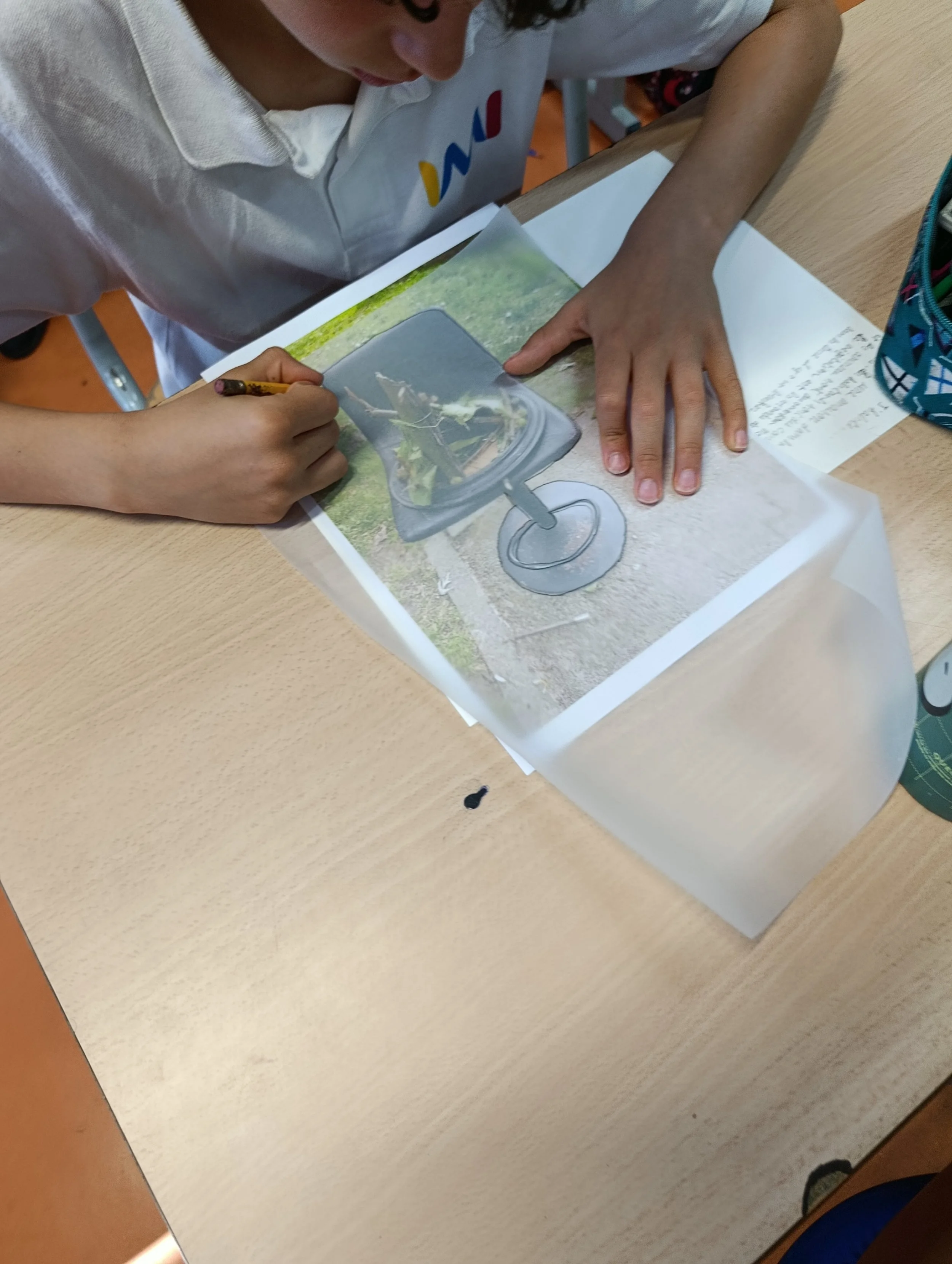 Un élève en train de faire une activité artistique ou scolaire avec une image d'une chaussure ou d'un objet en plastique sur du papier.