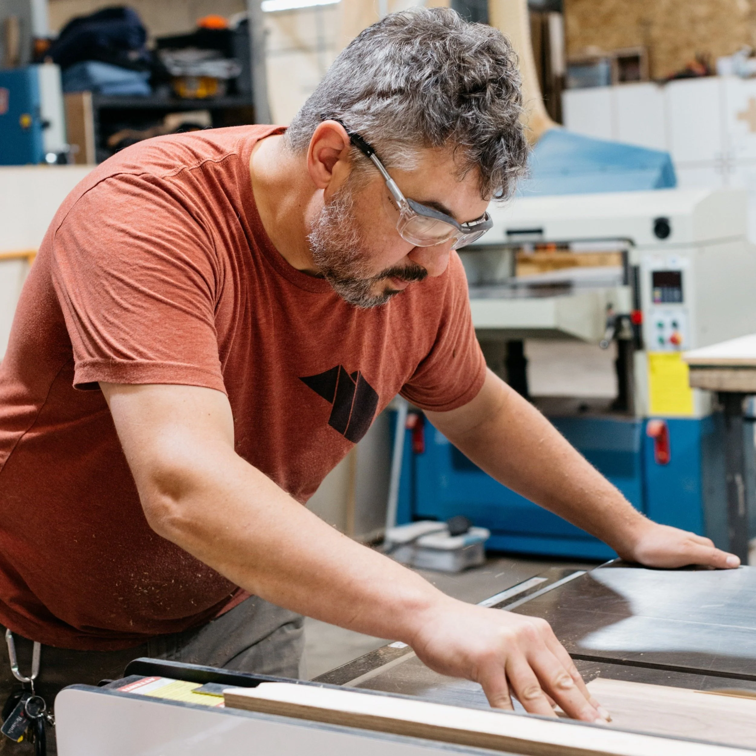 A man wearing safety glasses working on a woodworking project in a workshop.