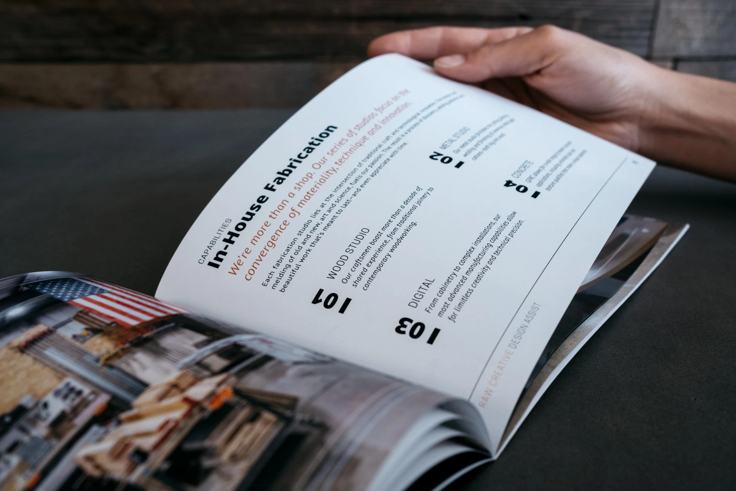 A person holding an open magazine, revealing a page about craftsmanship and woodworking. The page discusses the company's dedication to quality, with sections titled 'In-House Fabrication,' 'Wood Studio,' and 'Digital,' and includes a photo of a workshop and American flags.