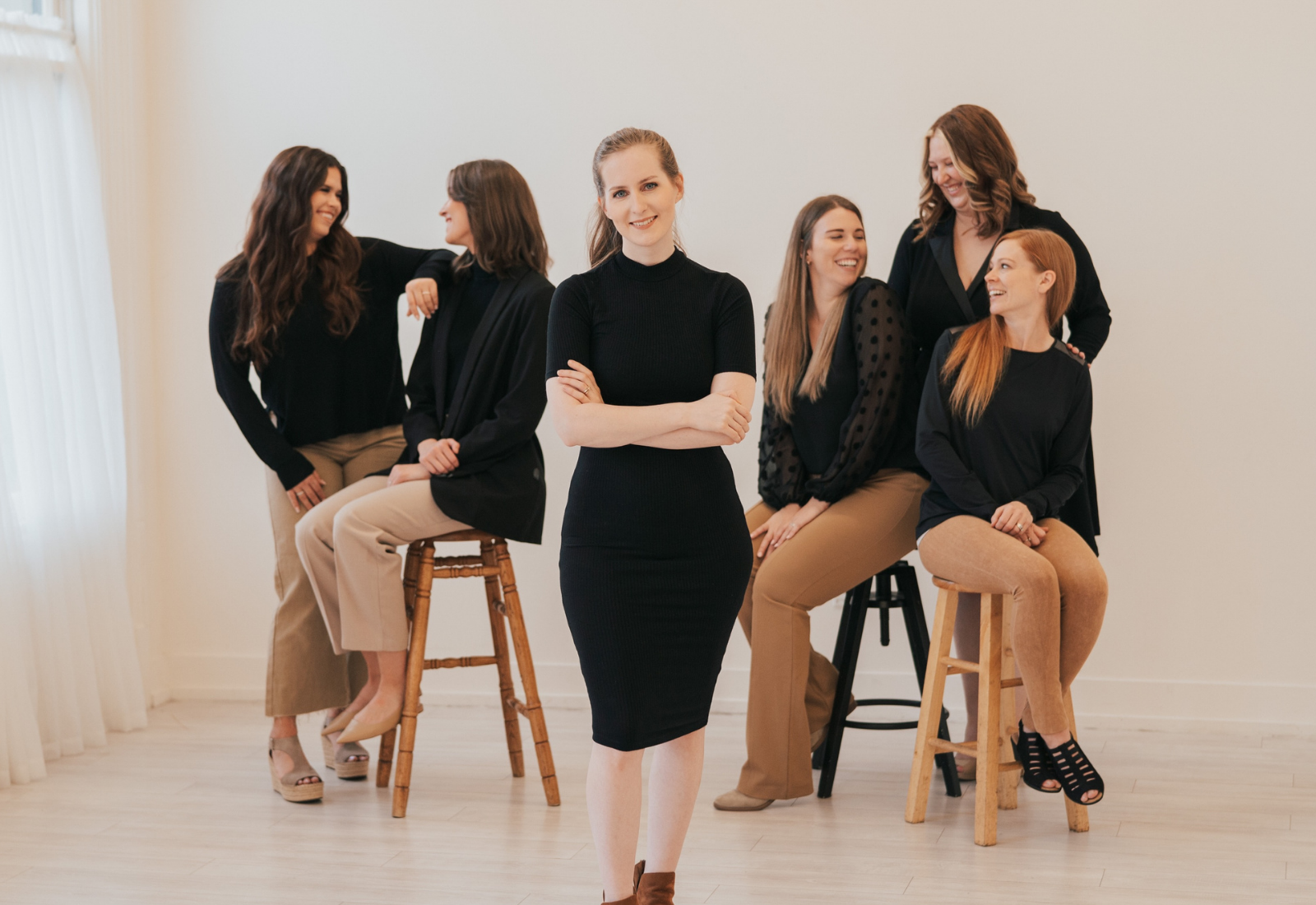 Gillian Perkins standing in a room with her arms crossed. She is smiling, and members of her team are sitting or standing in the room behind her, smiling and talking.