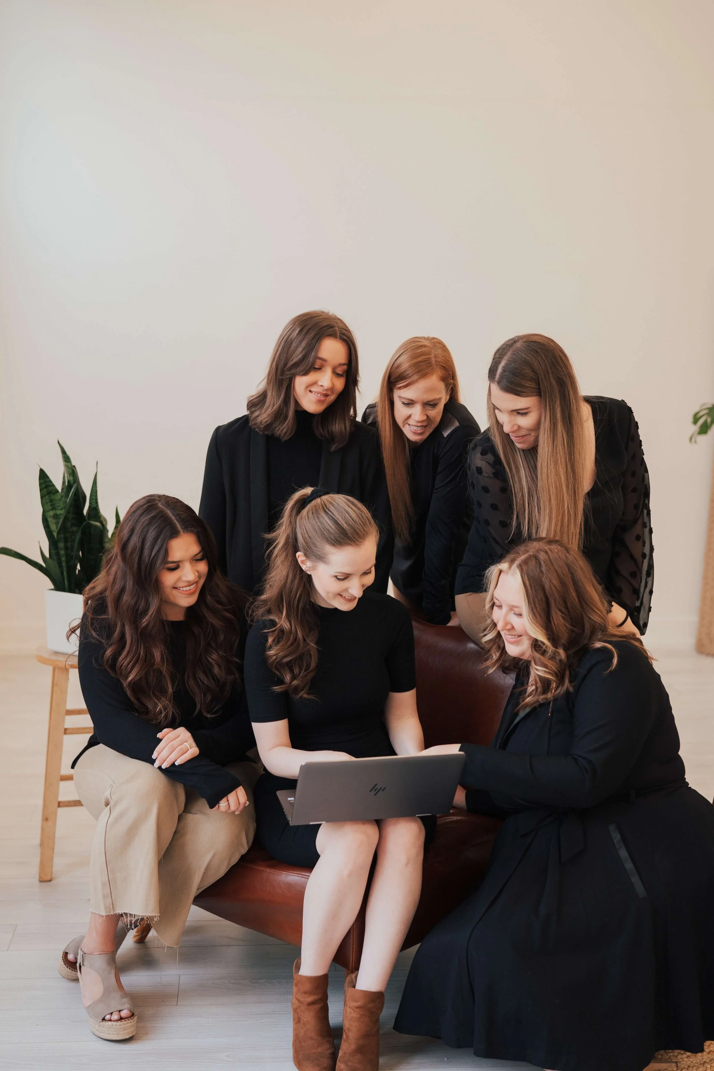 Gillian Perkins sitting on a chair, pointing at a laptop surrounded by her team, who are looking at the screen. Everyone is smiling.