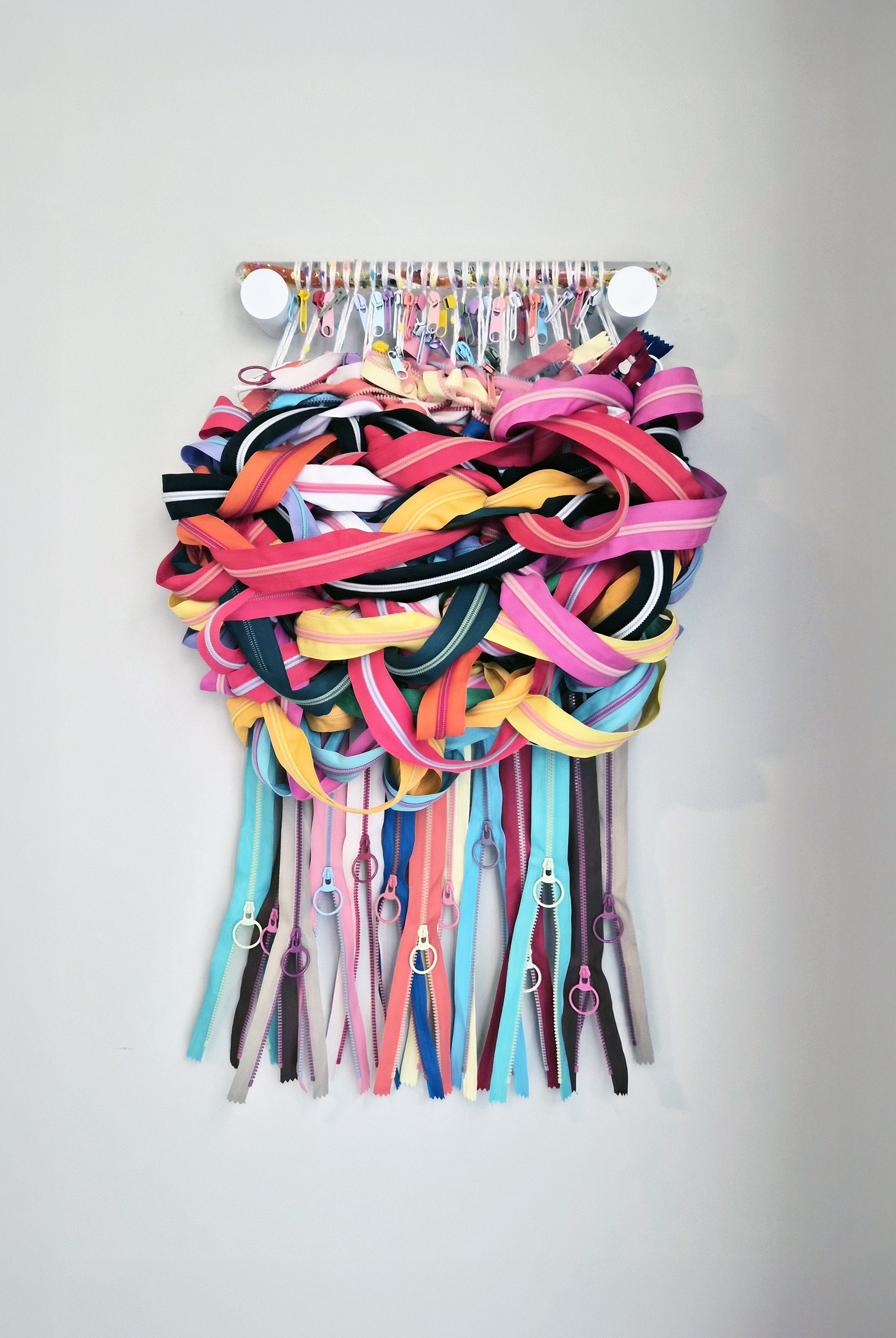 Fiber art comprised of interwoven zippers and zipper heads suspended from a translucent sensory wand