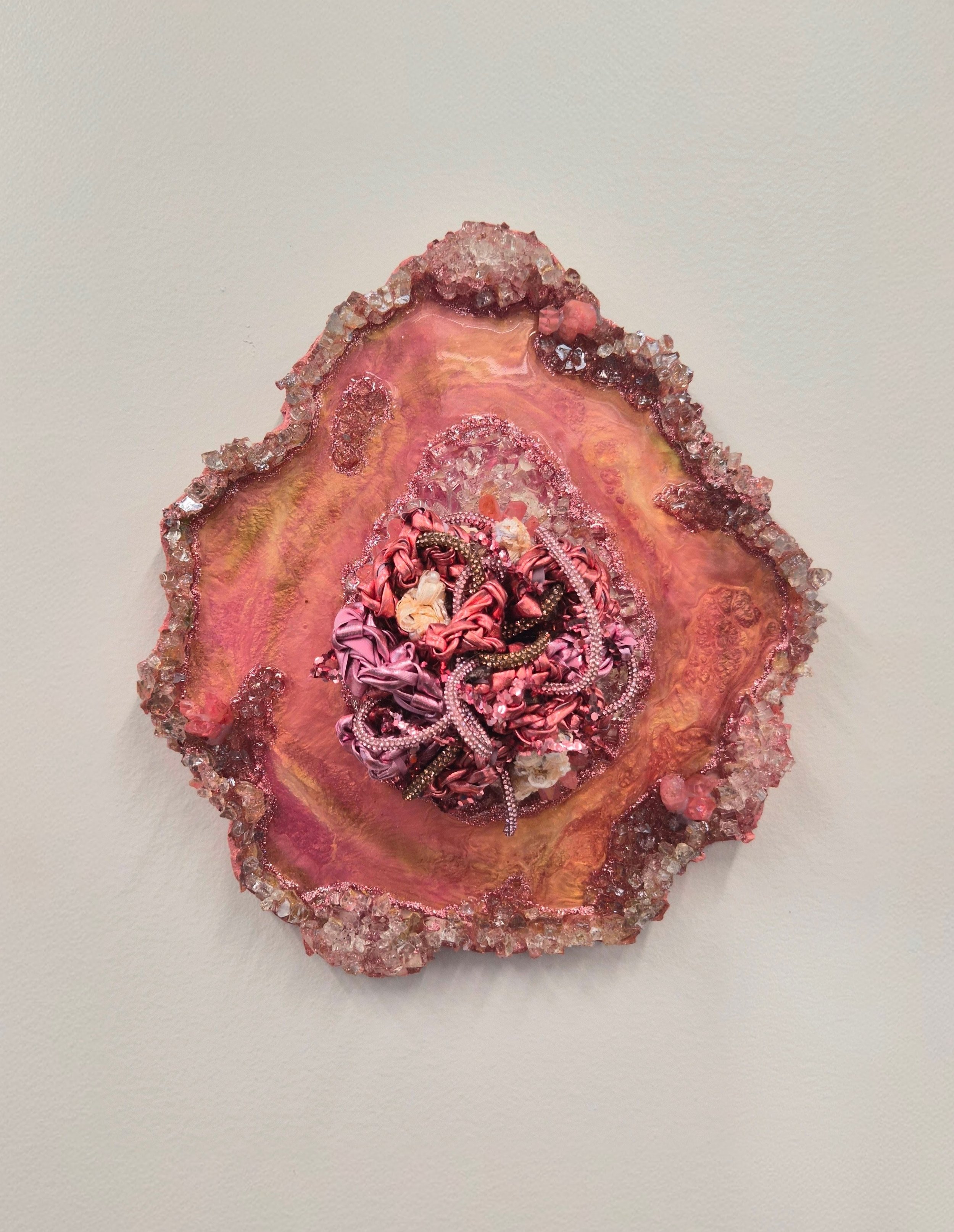 A fiber art piece comprised of interwoven fibers embedded in a resin geode with quartz, crushed glass, fire glass, mica powders, and glitter
