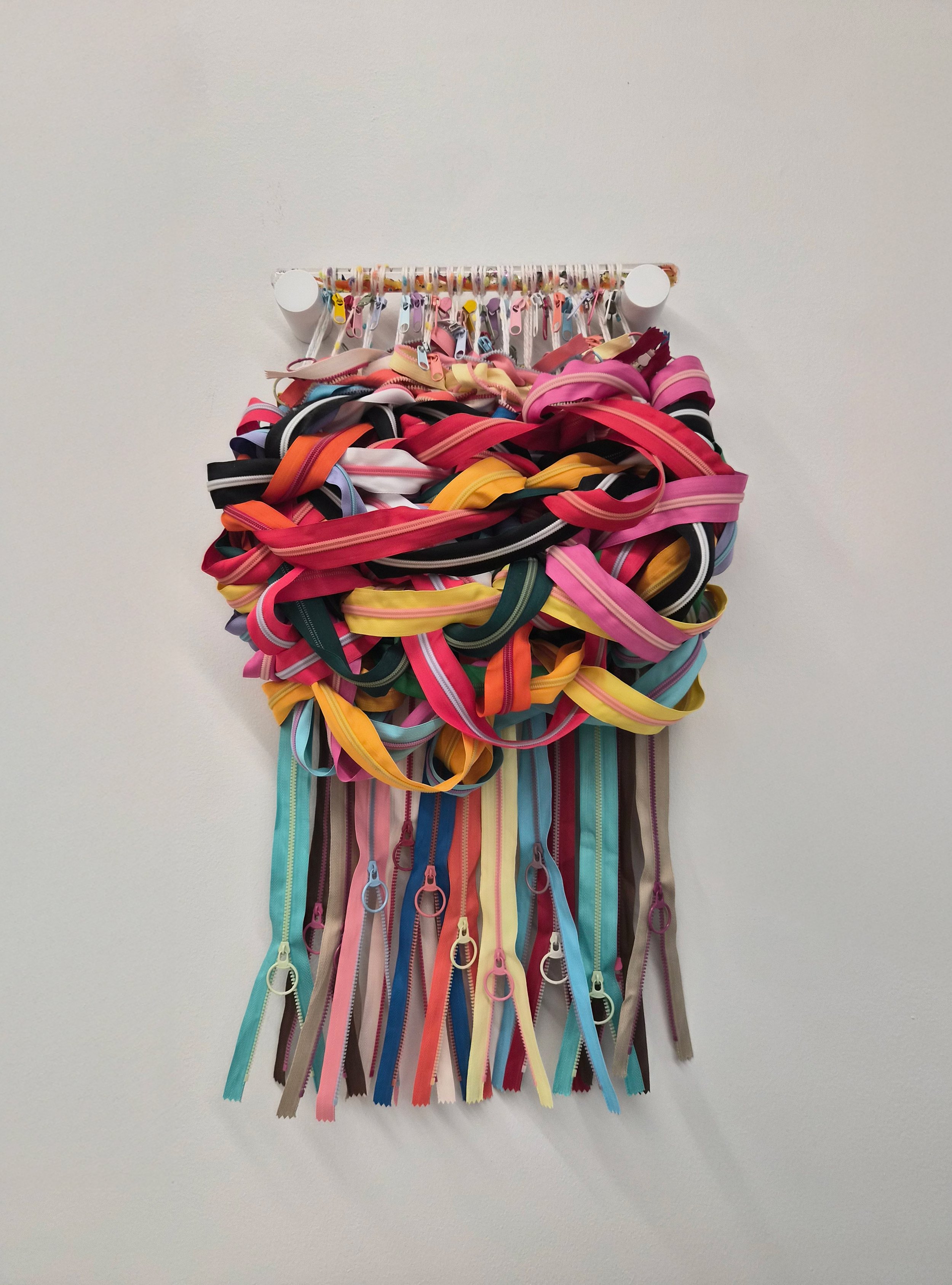 Fiber art comprised of interwoven zippers and zipper heads suspended from a translucent sensory wand