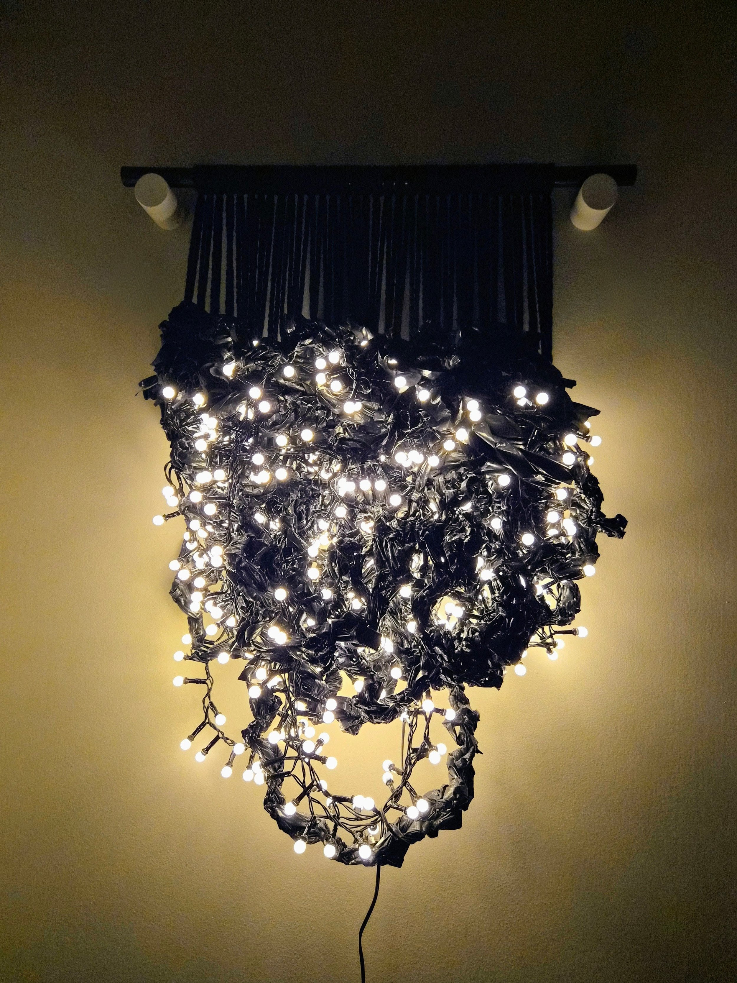 A fiber art piece comprised of interwoven trash bags and LED lights suspended from an acrylic dowel