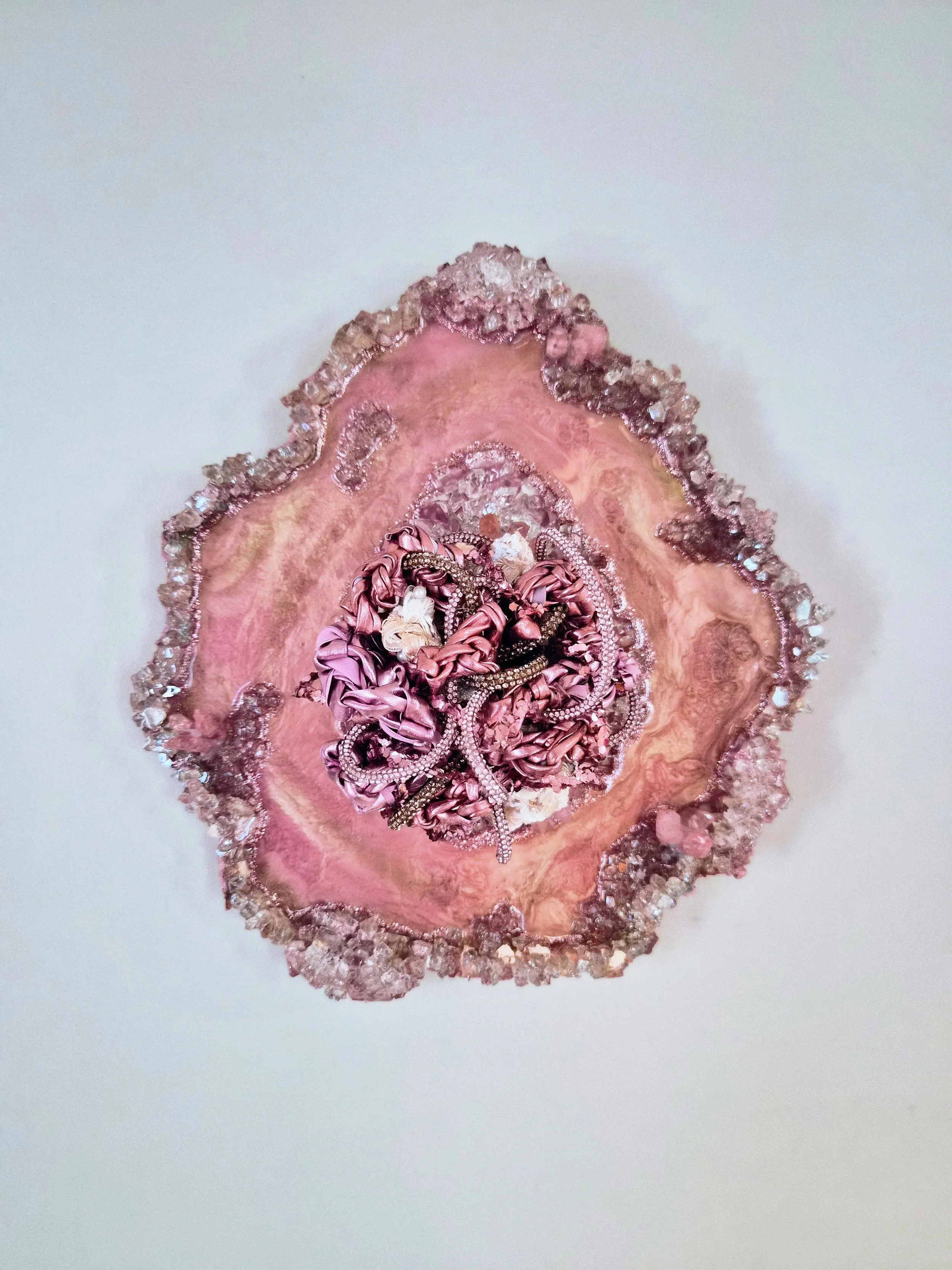 A fiber art piece comprised of interwoven fibers embedded in a resin geode with quartz, crushed glass, fire glass, mica powders, and glitter (resin geode by Emily Goff)