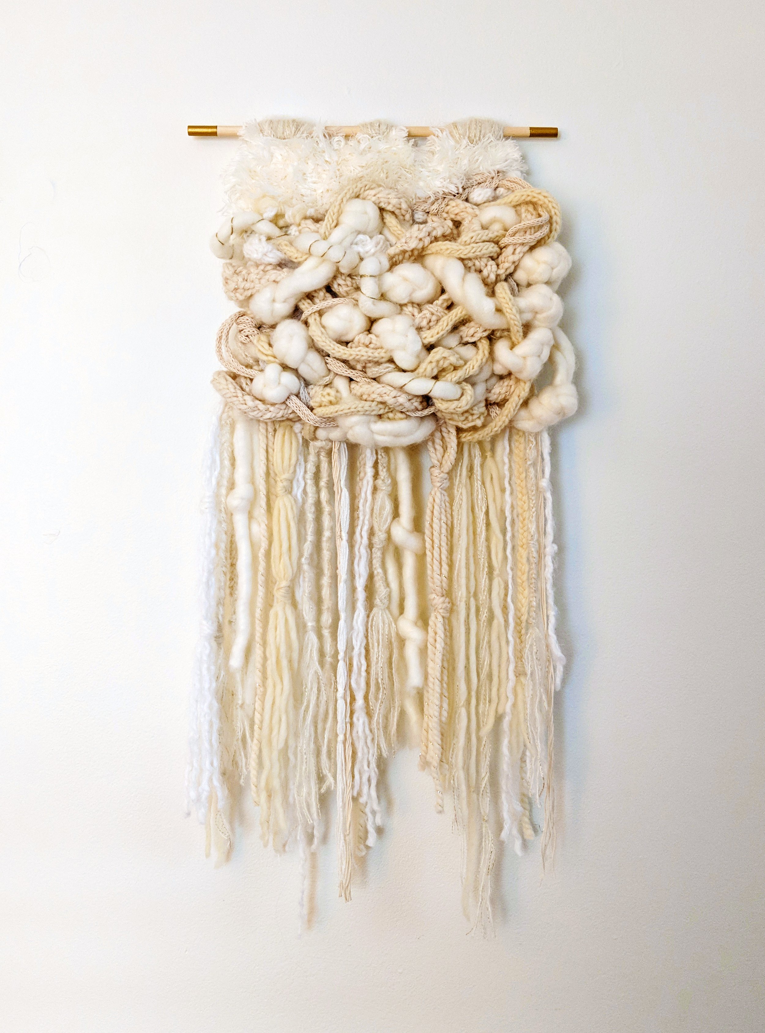 A fiber art piece comprised of interwoven fibers suspended from a wooden dowel with painted edges