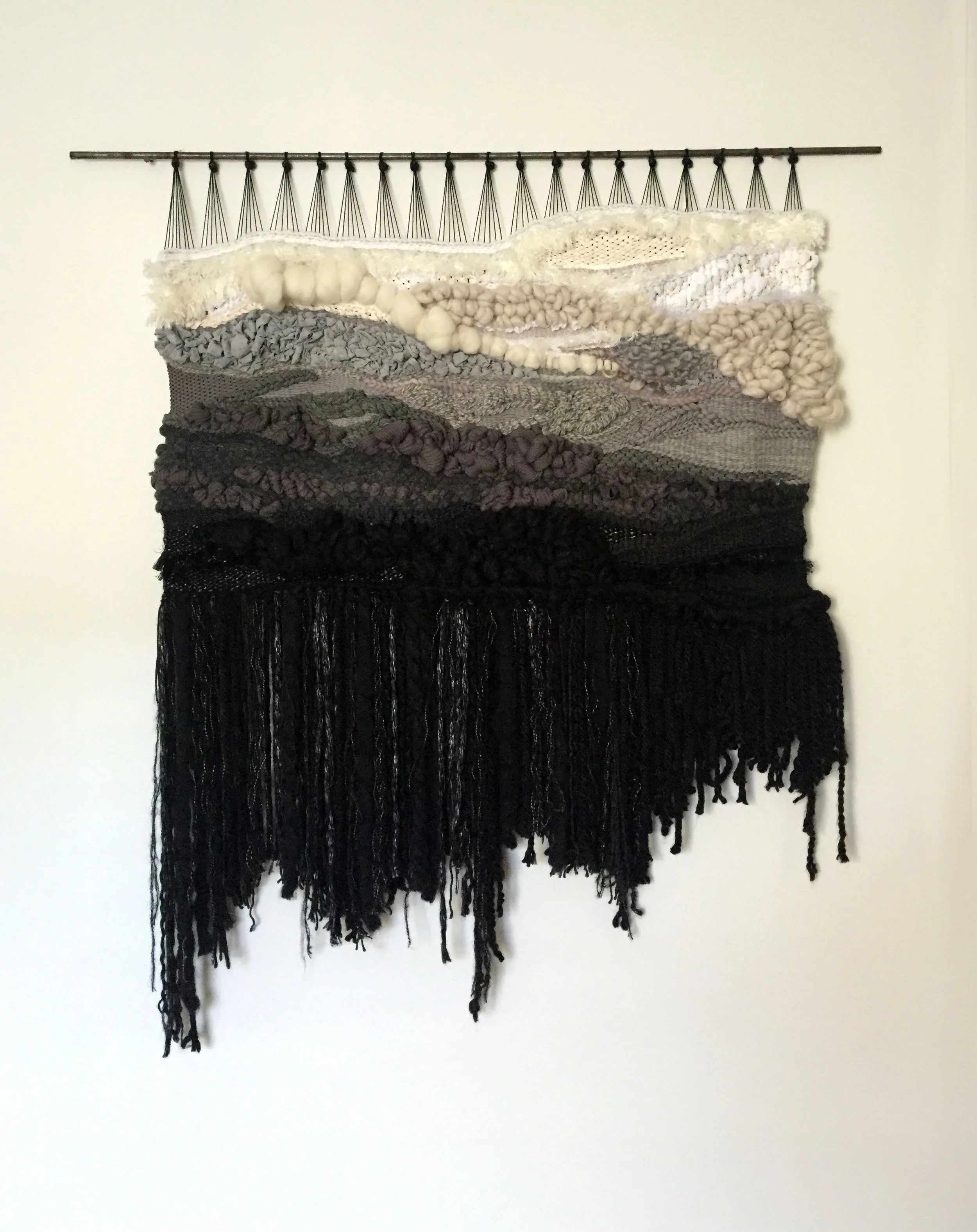 A fiber art piece comprised of interwoven fibers suspended from a steel dowel