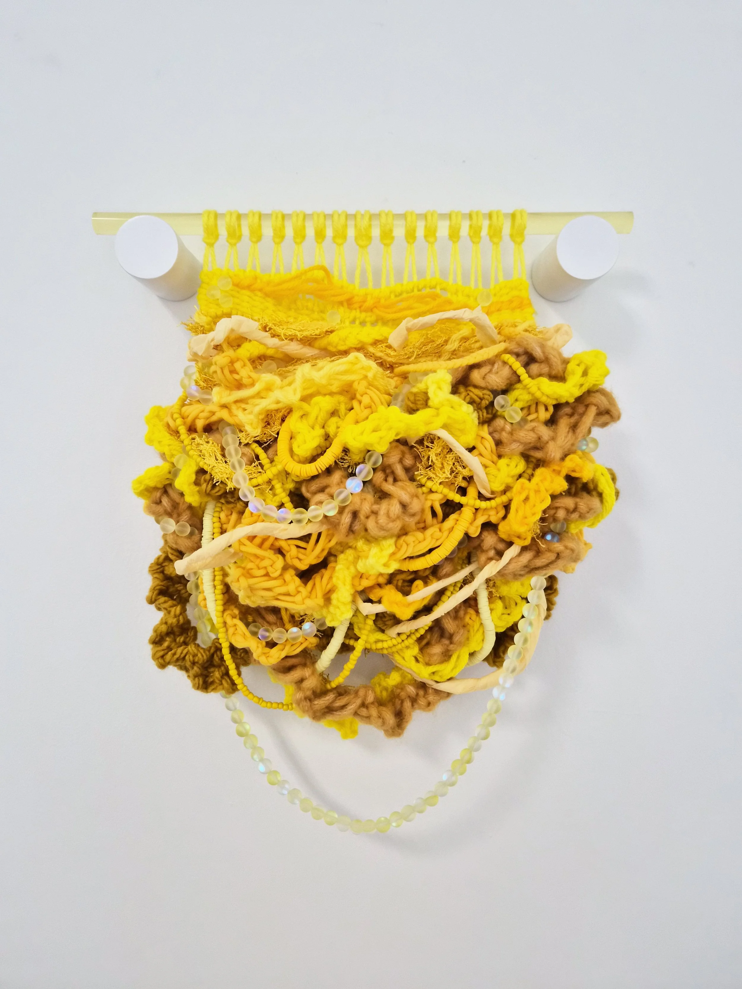 A composition of interwoven fibers, beads, and paper suspended from a translucent acrylic dowel