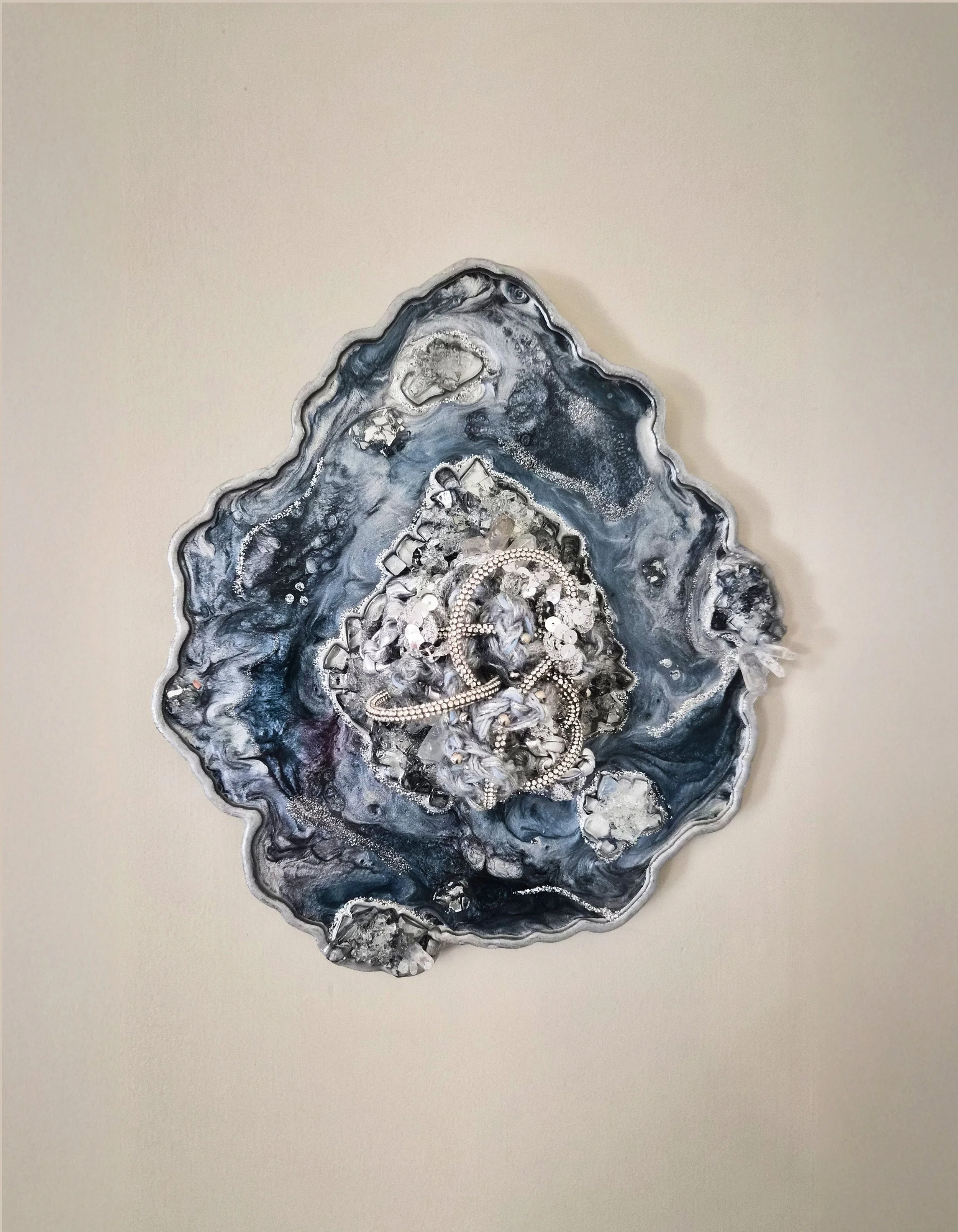 A fiber art piece comprised of interwoven fibers embedded in a resin geode with quartz, crushed glass, fire glass, mica powders, and glitter (resin geode by Emily Goff)