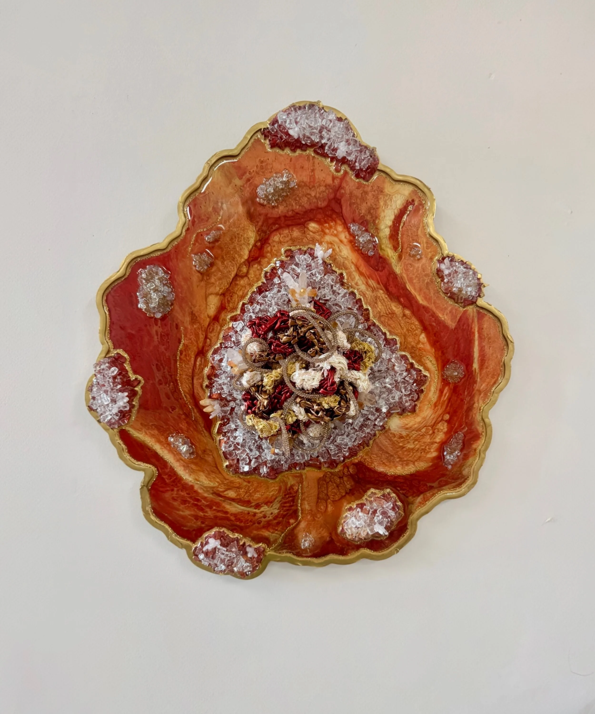 A fiber art piece comprised of interwoven fibers embedded in a resin geode with quartz, crushed glass, fire glass, mica powders, and glitter