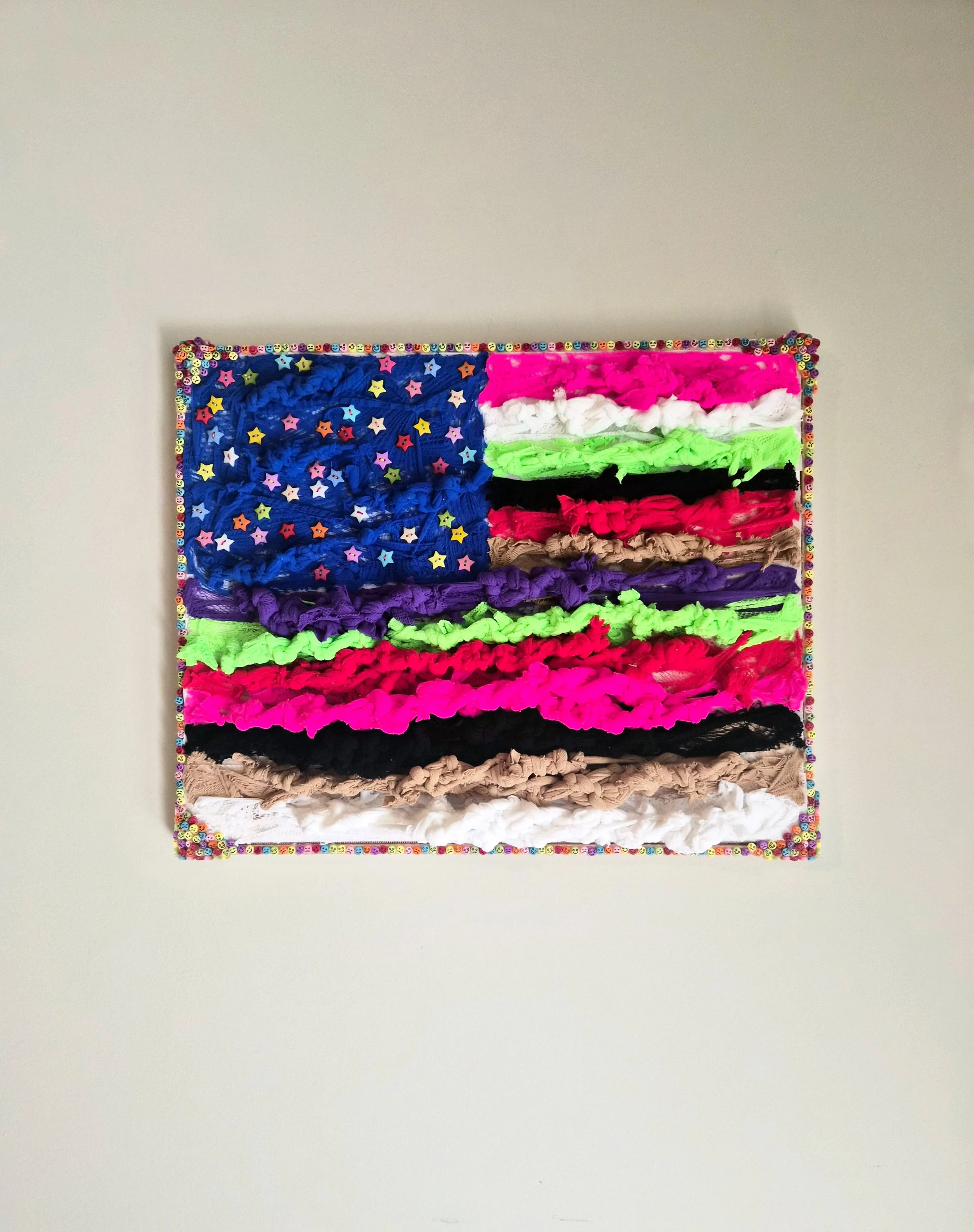 A composition of interwoven panty hose and buttons mounted to a Velcro frame surrounded by emoji beads