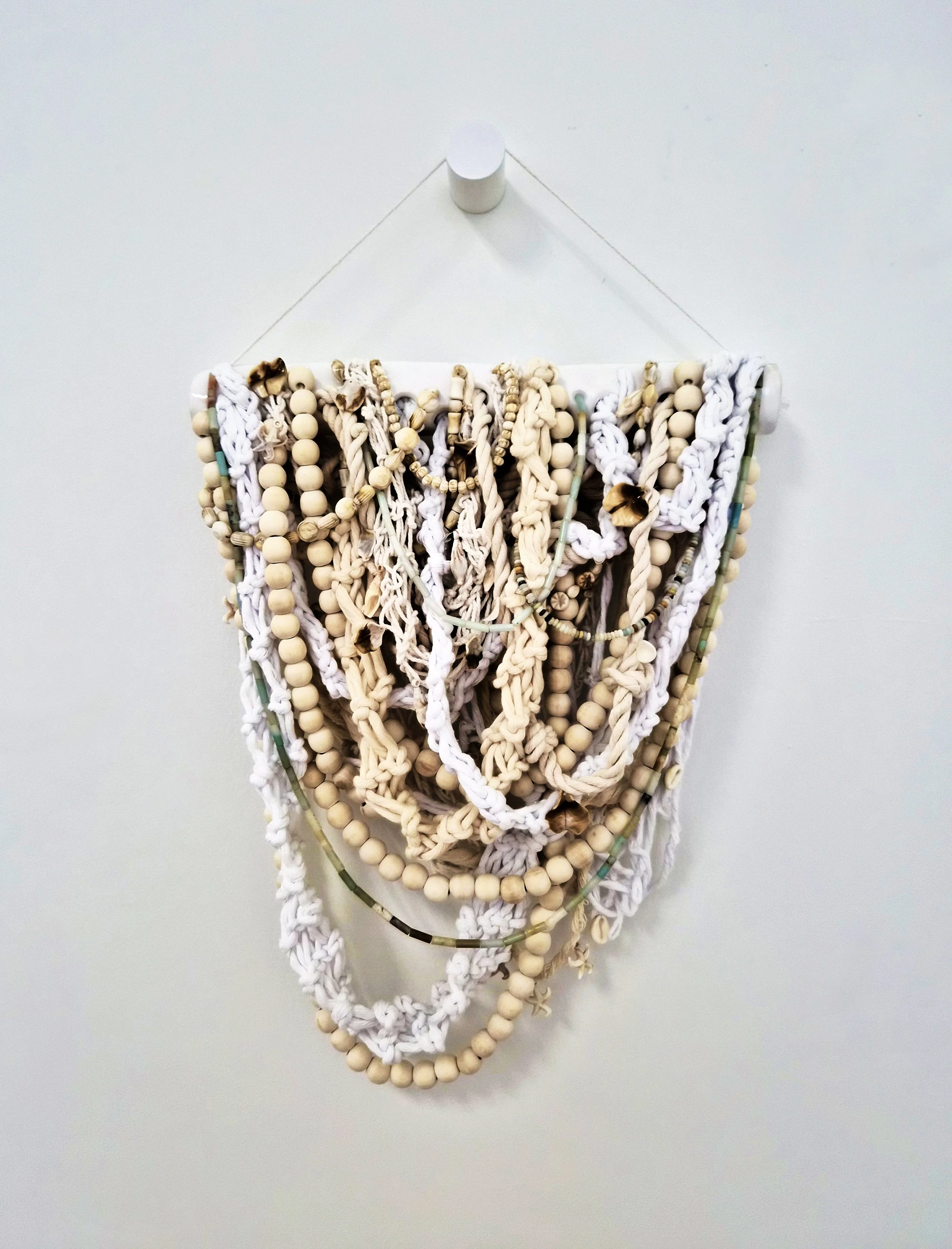 A composition of interwoven fibers, seashells, and beads suspended from a ceramic dowel (ceramic dowel by Tracy Kepley)