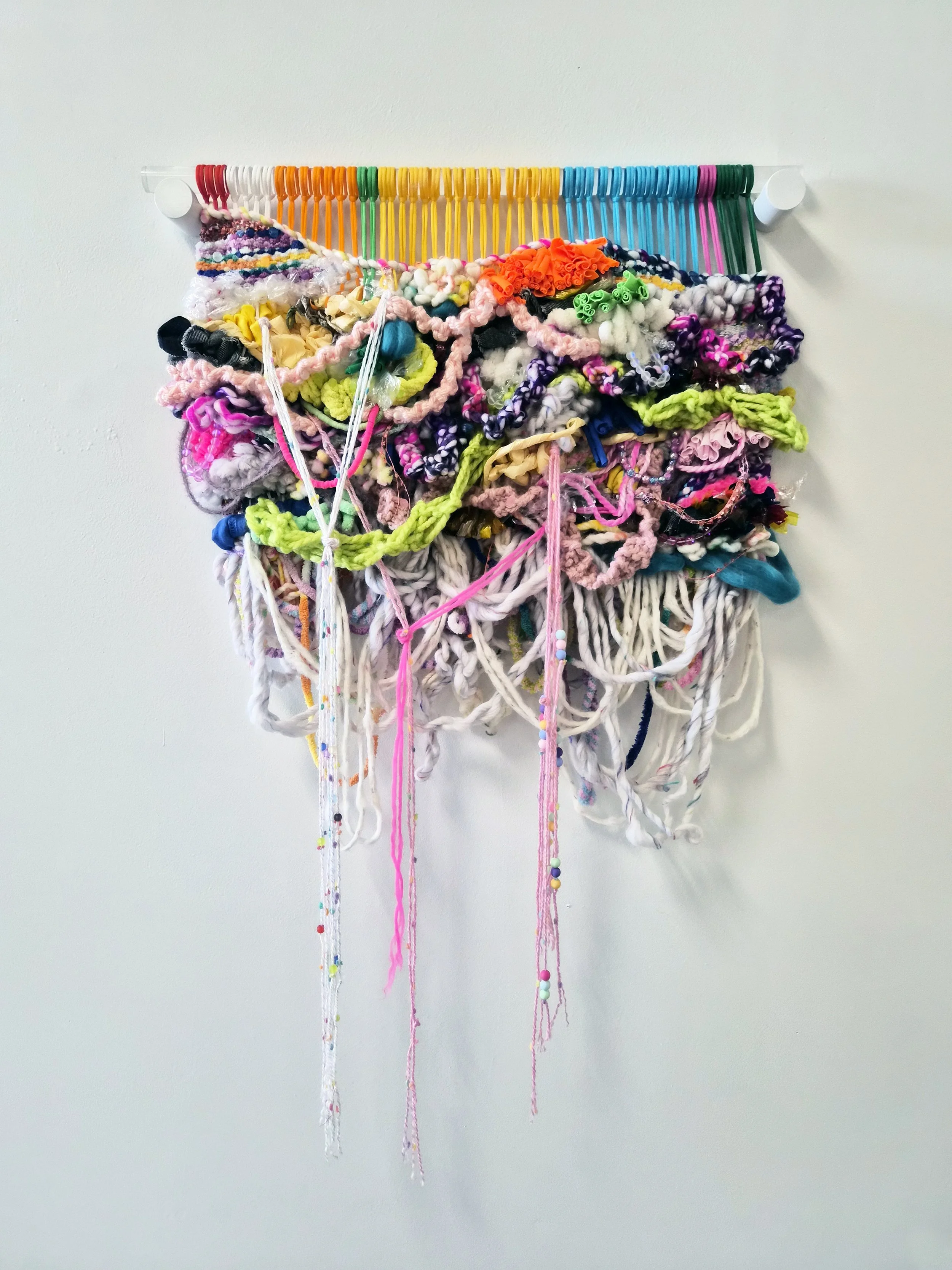 A fiber art piece comprised of interwoven fibers, beads, and paper suspended from a translucent acrylic dowel