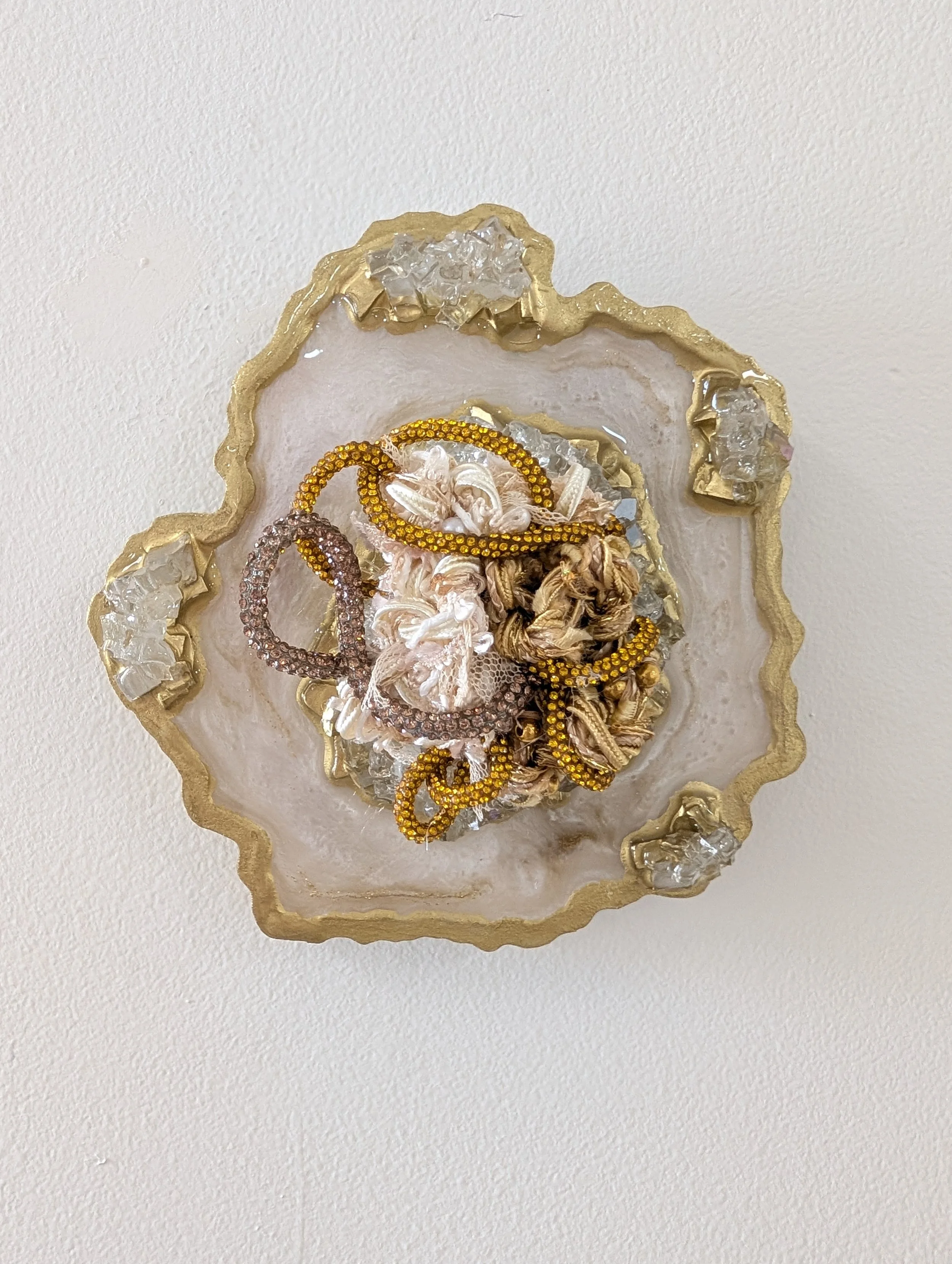 A fiber art piece comprised of interwoven fibers embedded in a resin geode with quartz, crushed glass, fire glass, mica powders, and glitter