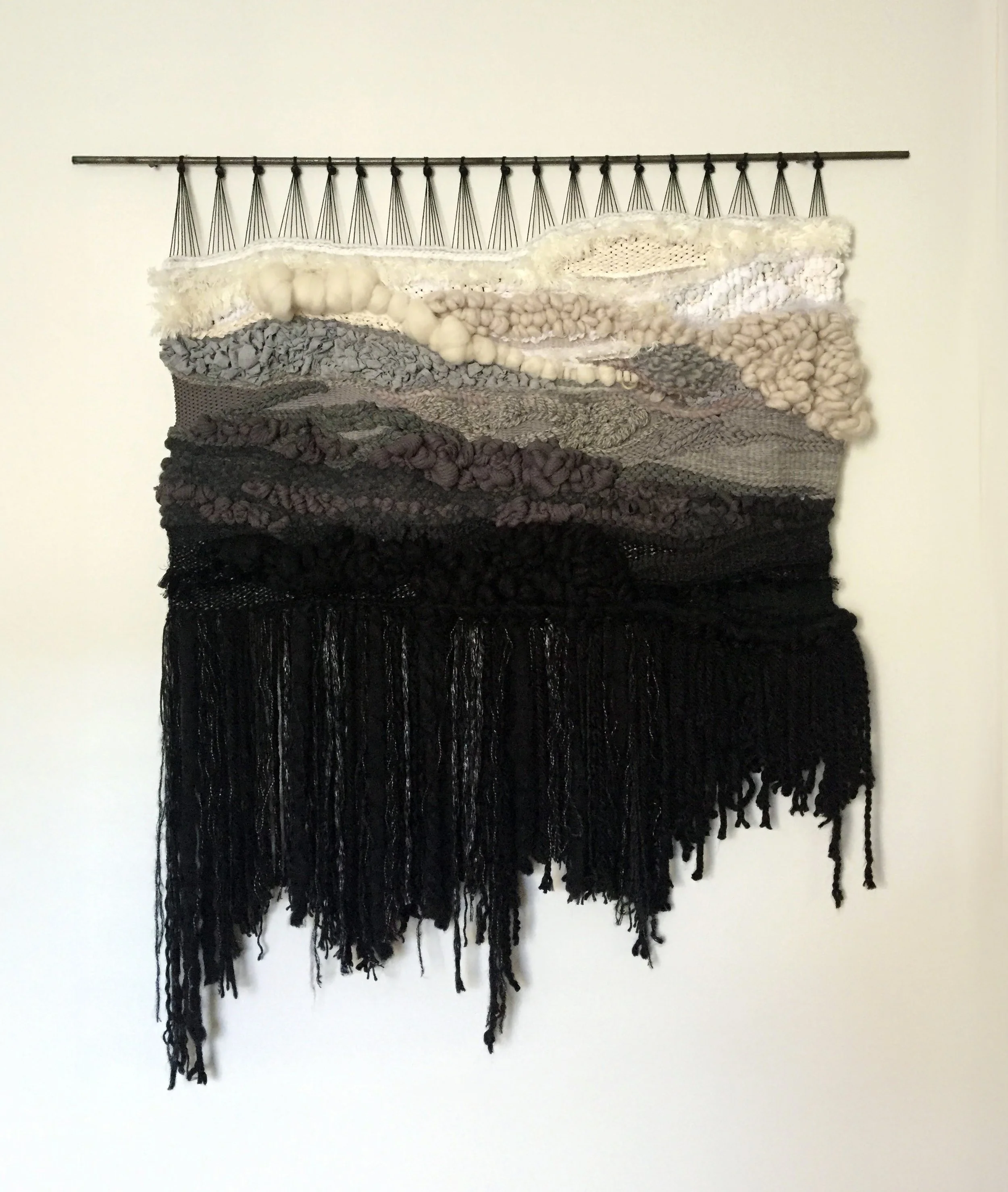 A fiber art piece comprised of interwoven fibers suspended from a steel dowel
