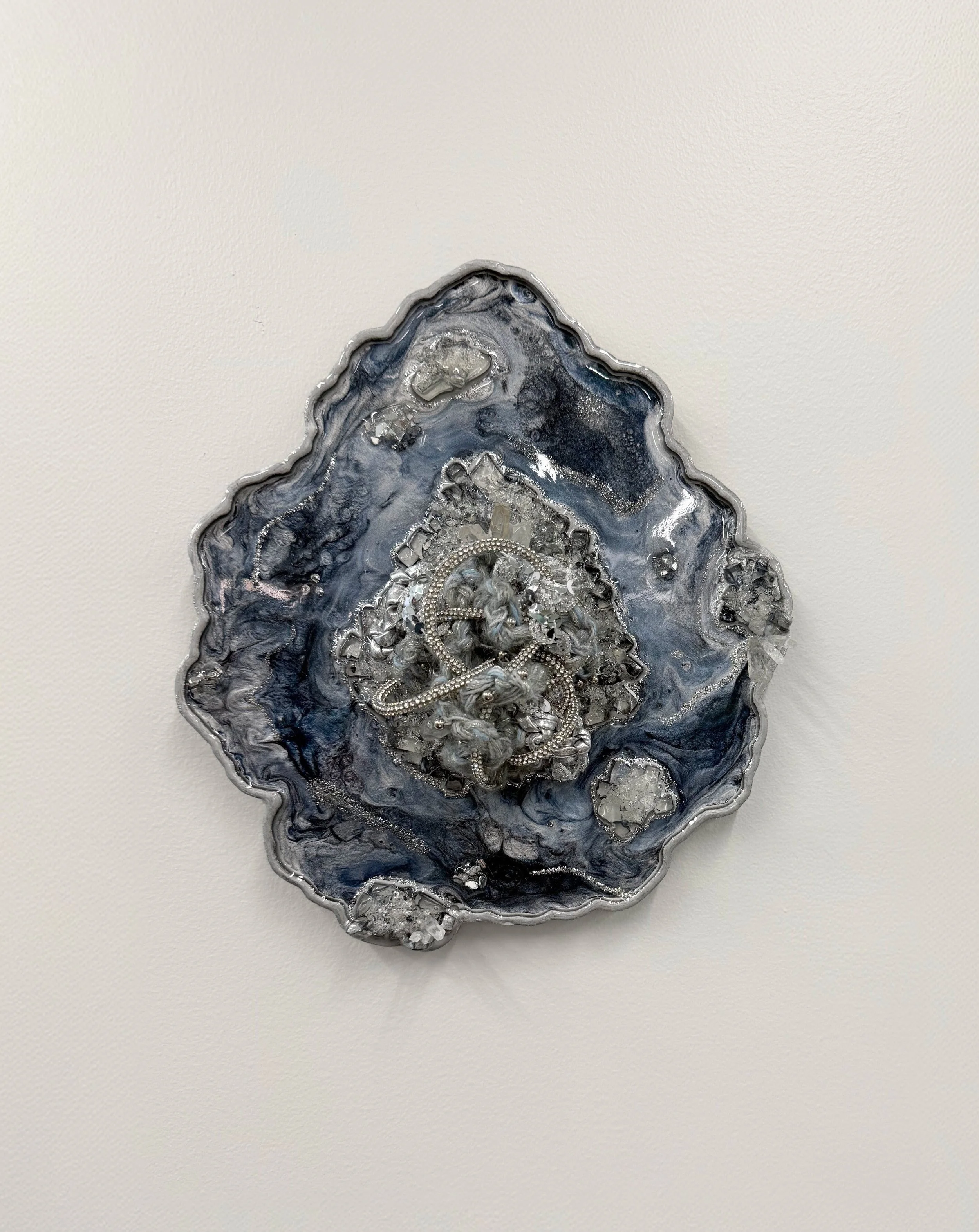 A fiber art piece comprised of interwoven fibers embedded in a resin geode with quartz, crushed glass, fire glass, mica powders, and glitter (resin geode by Emily Goff)