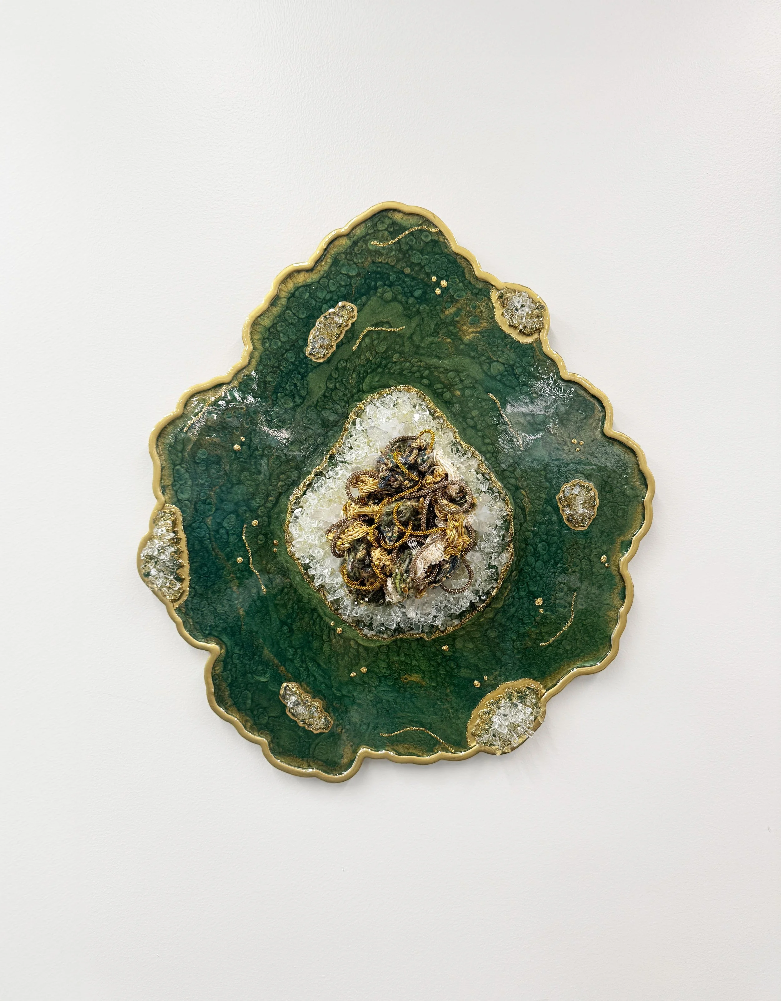 A fiber art piece comprised of interwoven fibers embedded in a resin geode with quartz, crushed glass, fire glass, mica powders, and glitter
