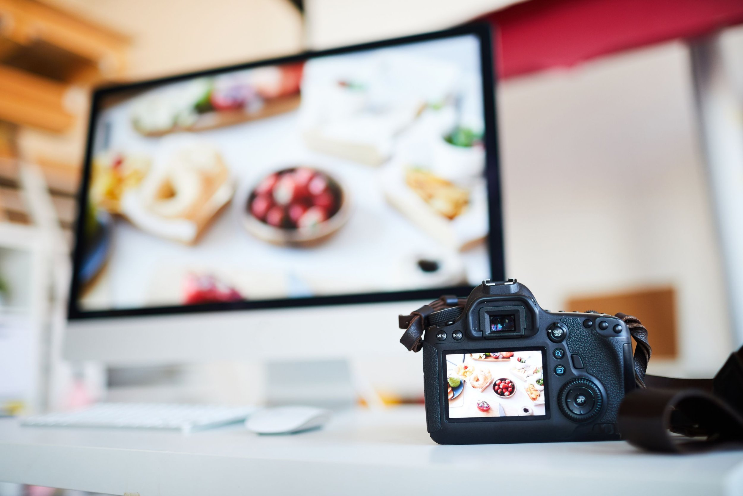 A camera on a desk capturing a computer monitor displaying a photo of assorted desserts and fruits.