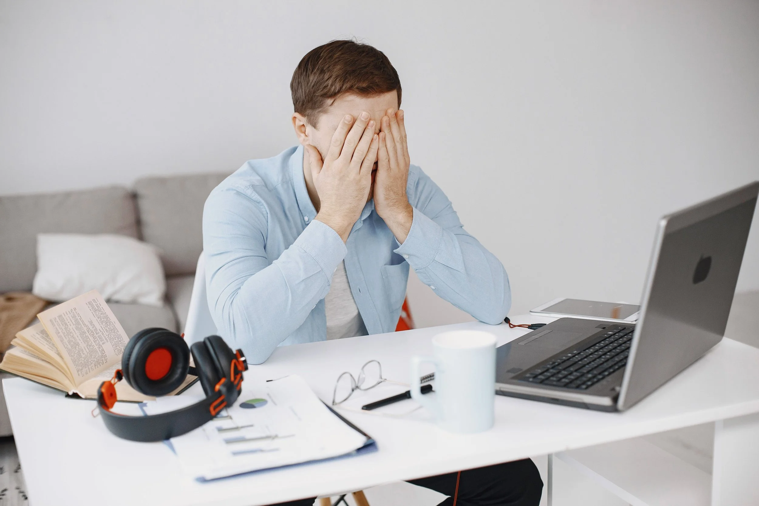 Person sitting at a desk with their face covered by their hands beside a laptop