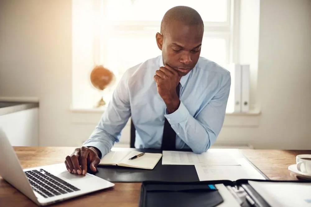 Man working at a desk with a laptop, notebook, and planning materials.