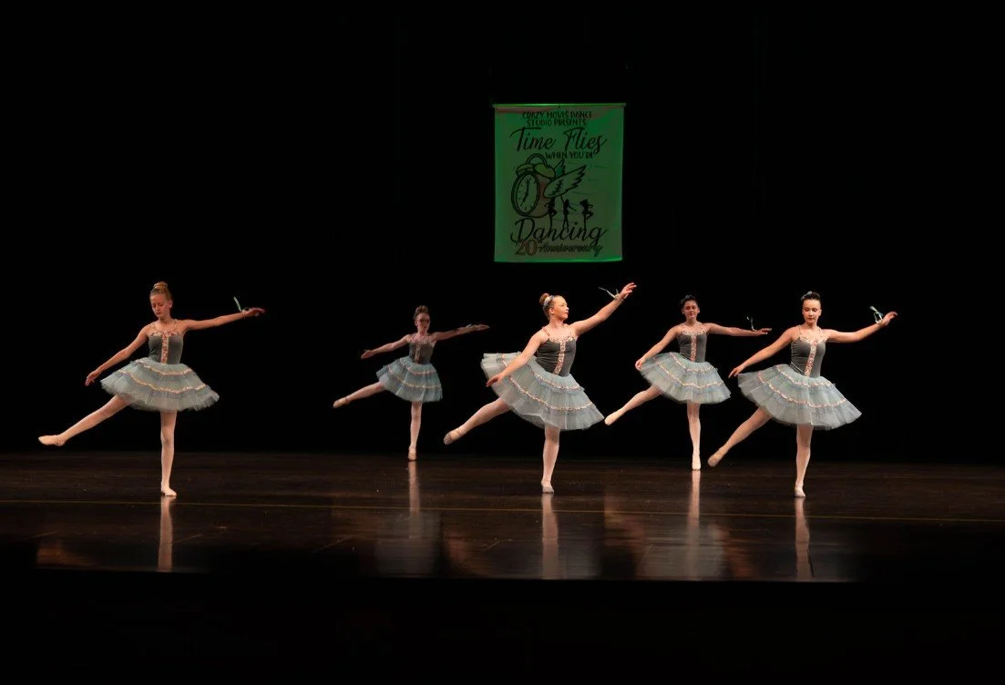 Group of young dancers striking a final pose on stage at a Crazy Moves Dance recital, wearing matching blue costumes and smiling confidently..jpg