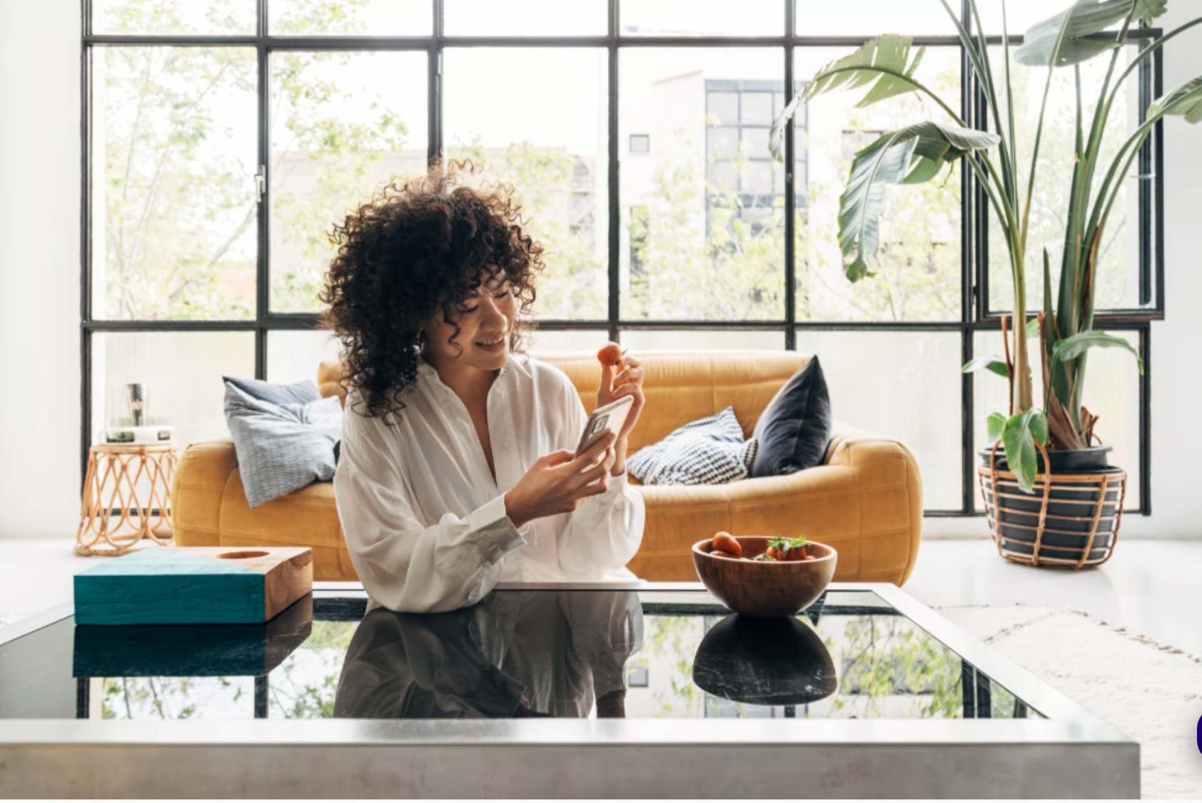 woman holding a strawberry in one hand a nd cell phone in other hand smiling