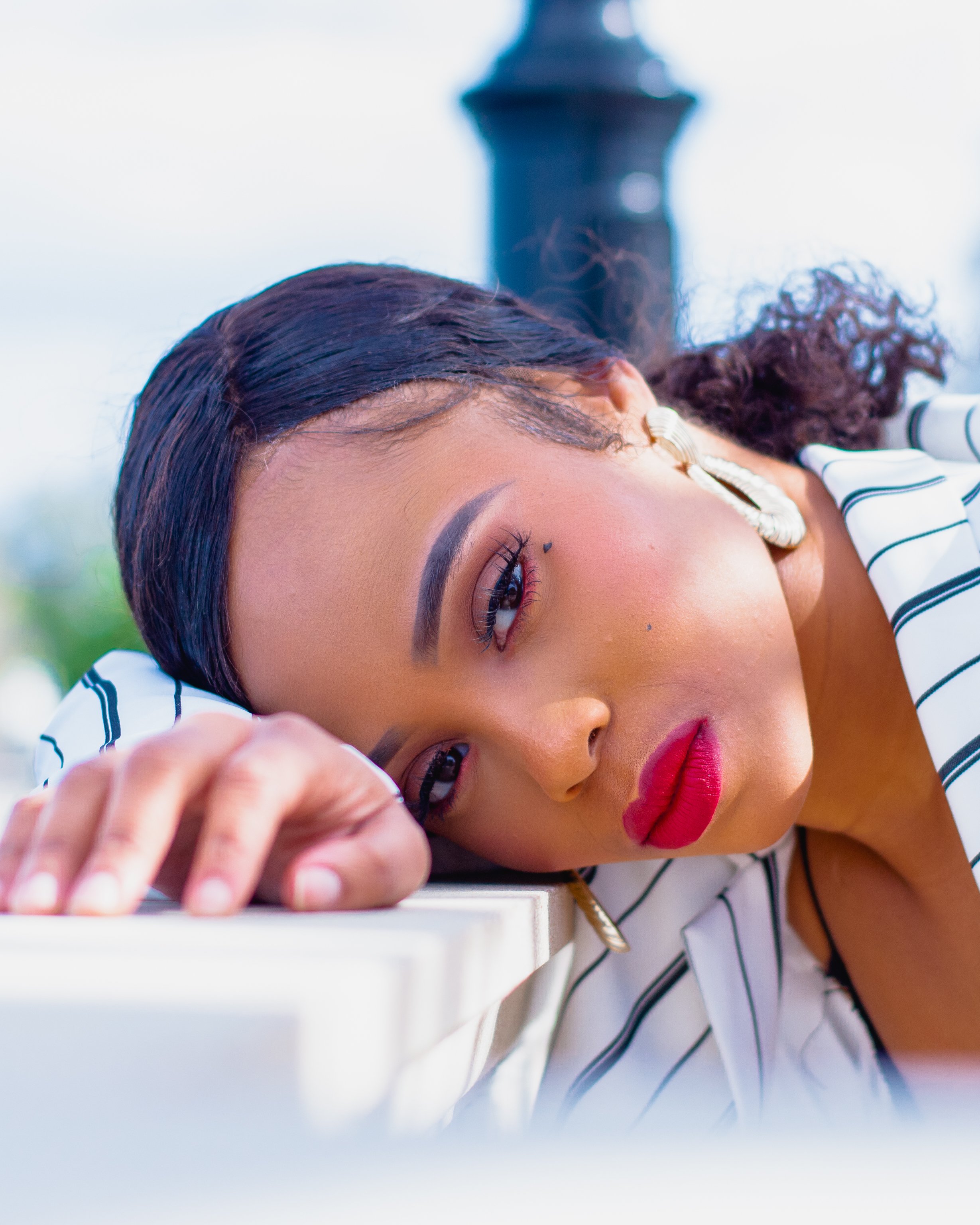 A woman with dark hair and makeup resting her head on a table, looking directly at the camera.