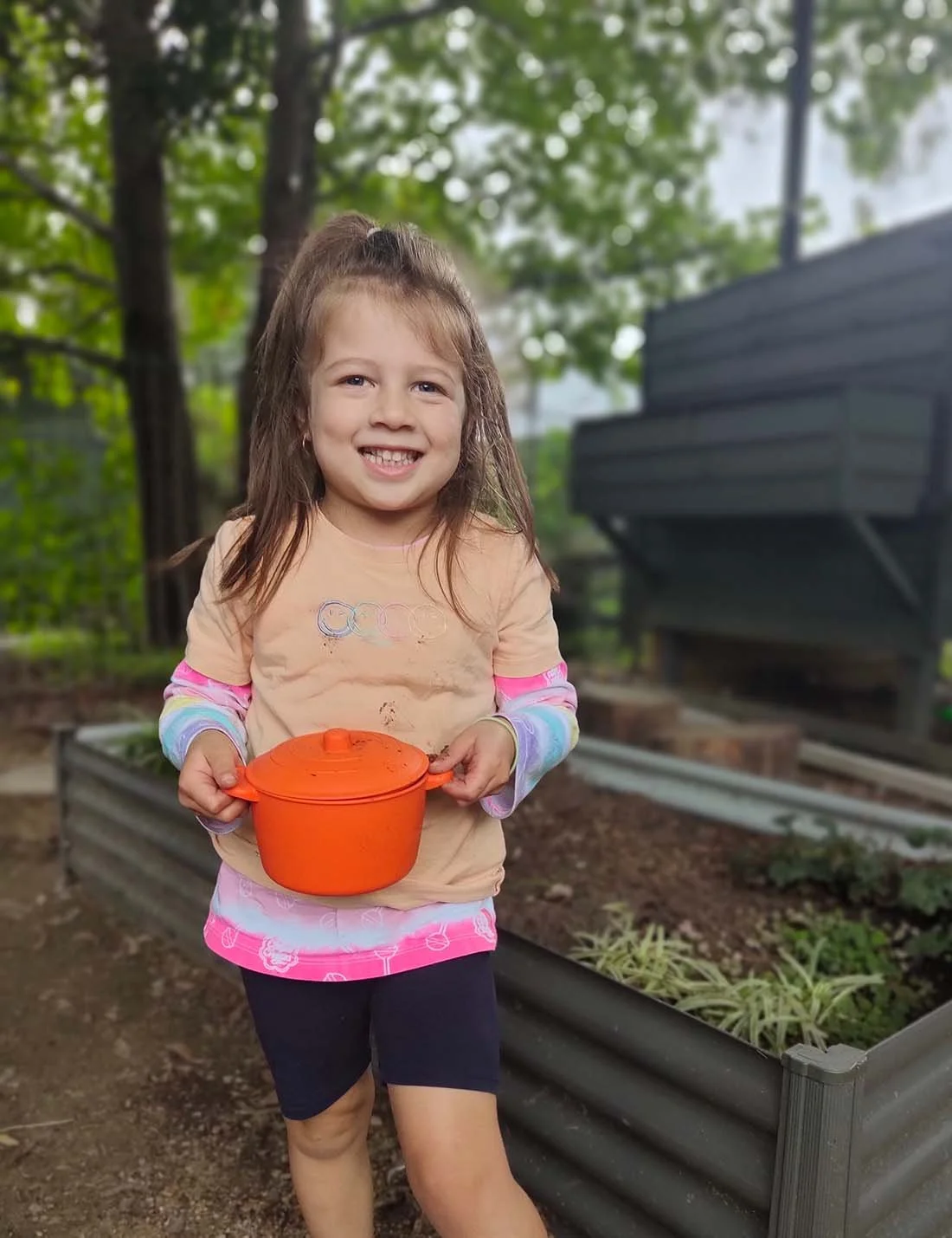 Little girl smiling in the garden holding an orange pot