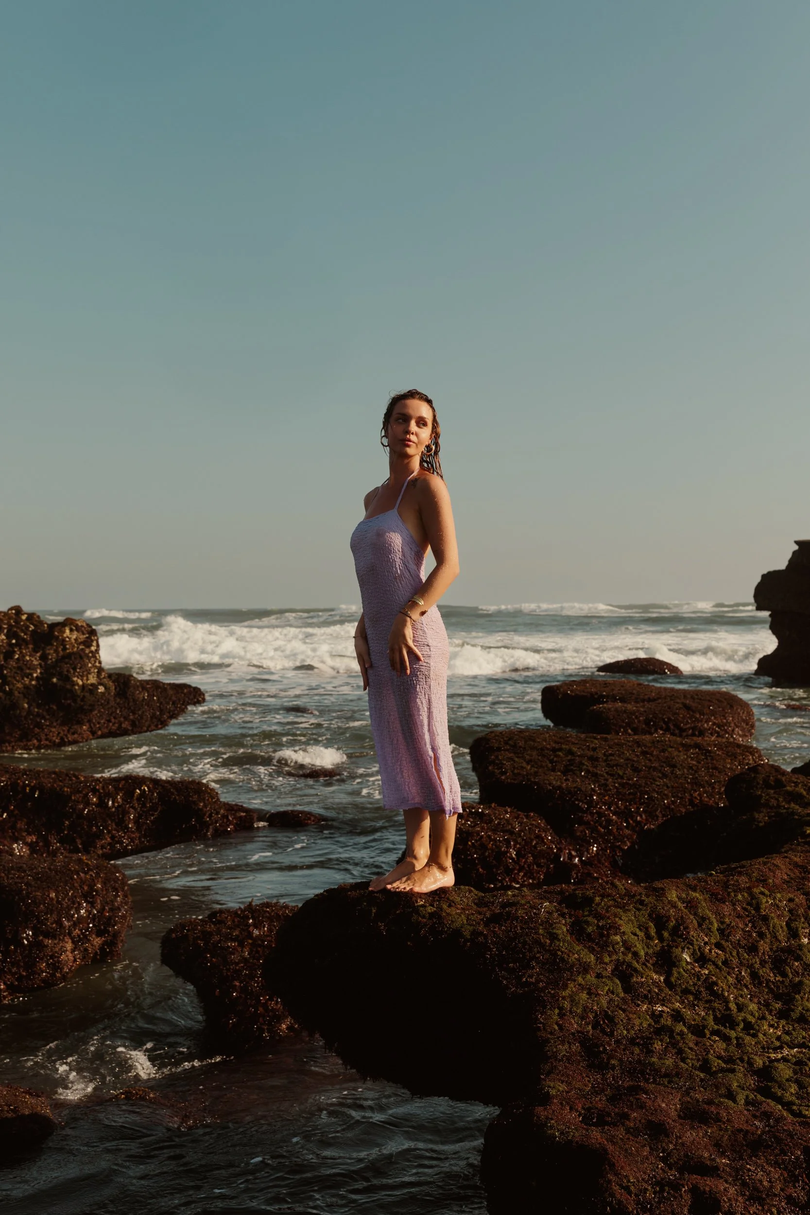Bali Photoshoot by Australian Photographer. Female stands on edge of rock with ocean in background