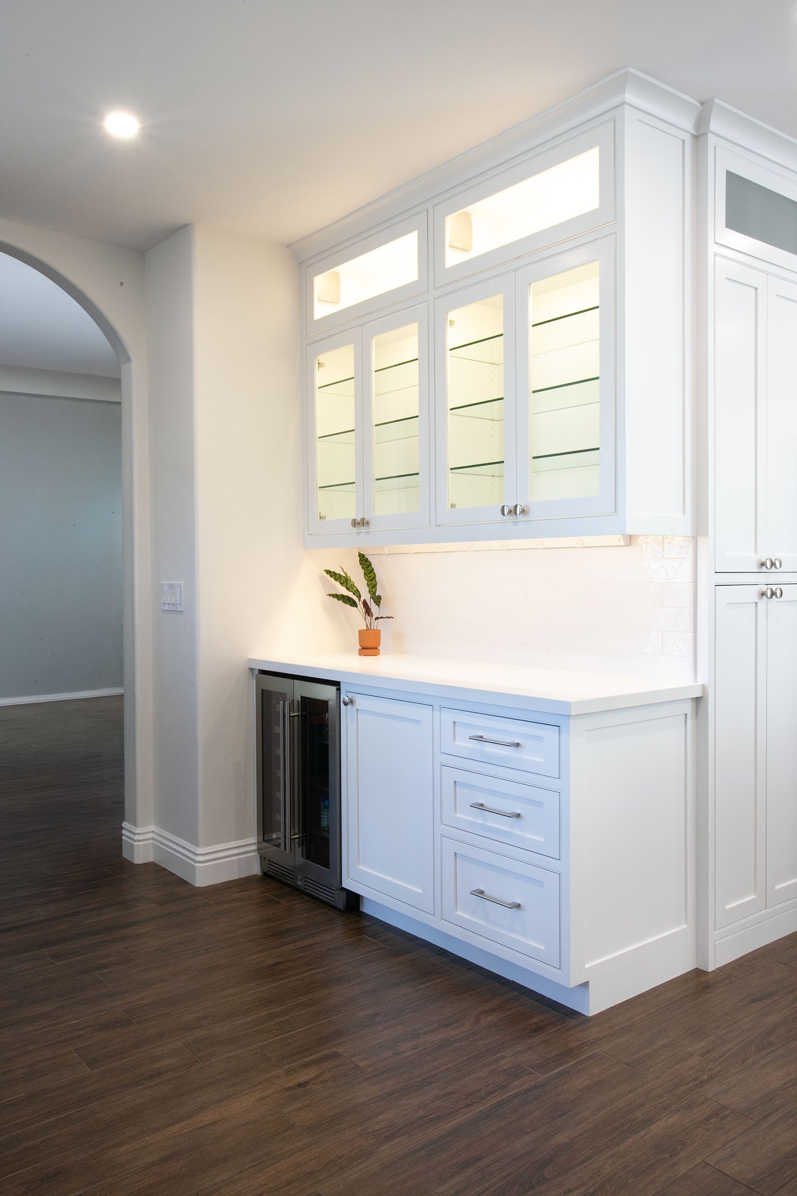 Custom kitchen bar area with lighted glass upper cabinets, beverage fridge, and white shaker cabinetry in Tehachapi, California