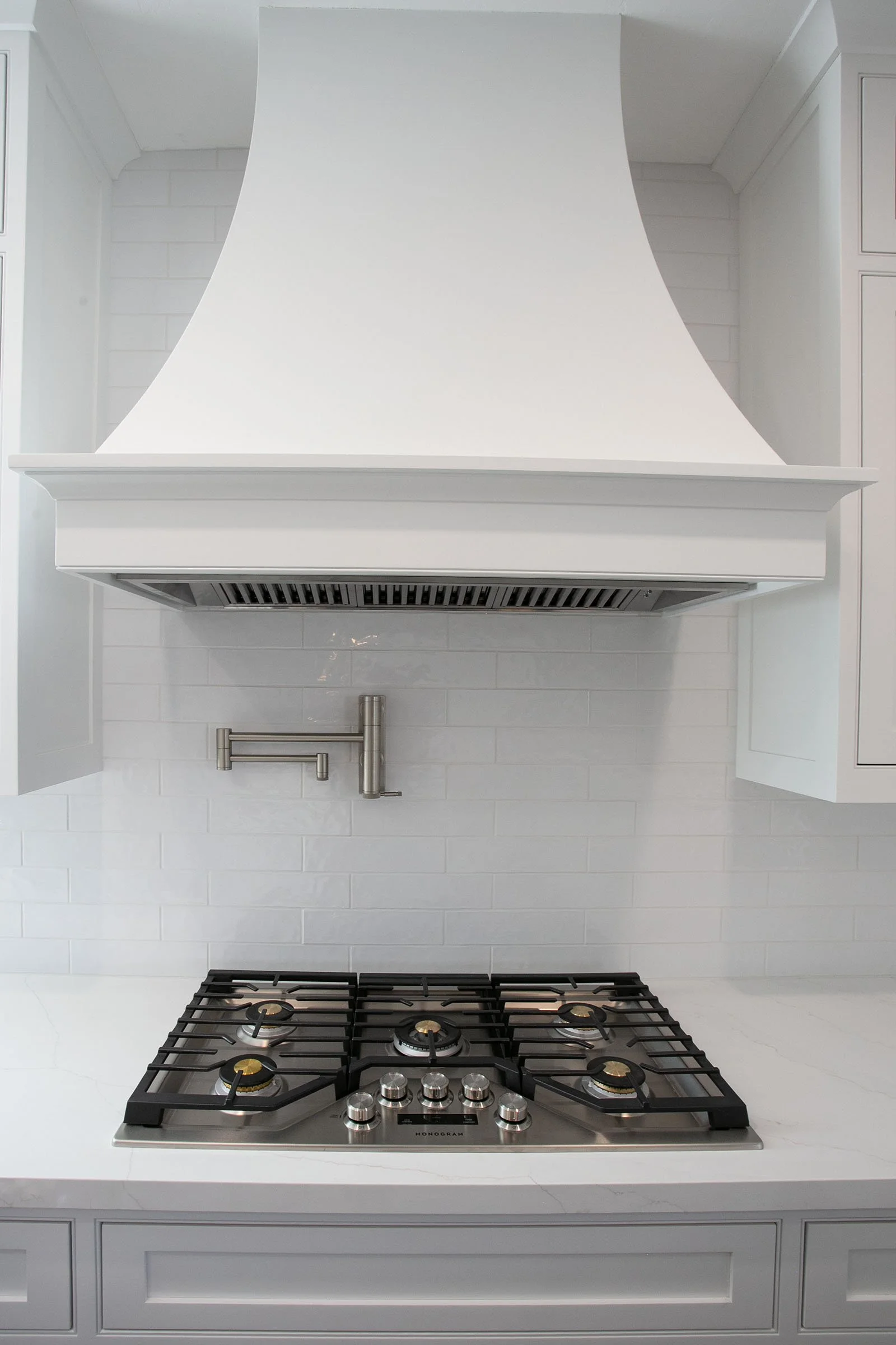 Custom range hood with white shaker cabinets, gas cooktop, and subway tile backsplash in Tehachapi, California