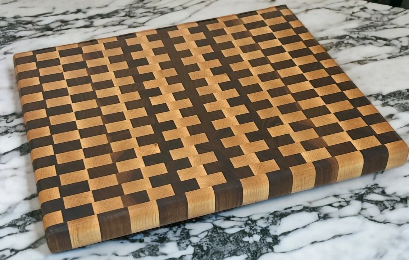 A wooden chessboard with a checkered pattern of light and dark wood squares, resting on a marble countertop.