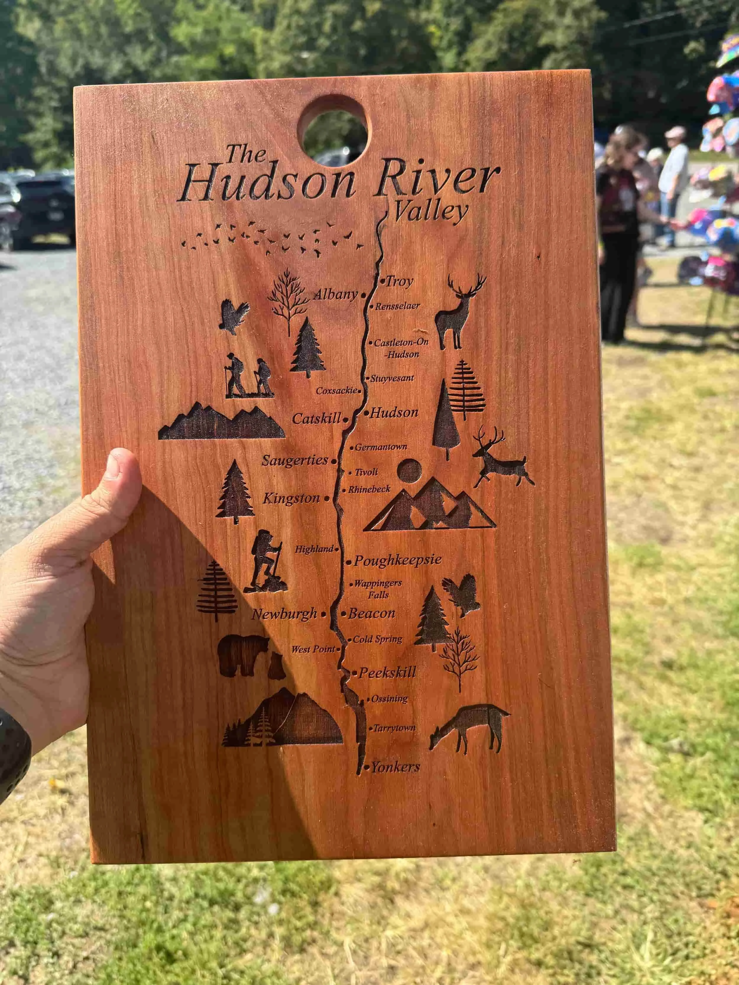 Wooden map of the Hudson River Valley with illustrations of mountains, trees, animals, and activities along the river, including towns and landmarks.