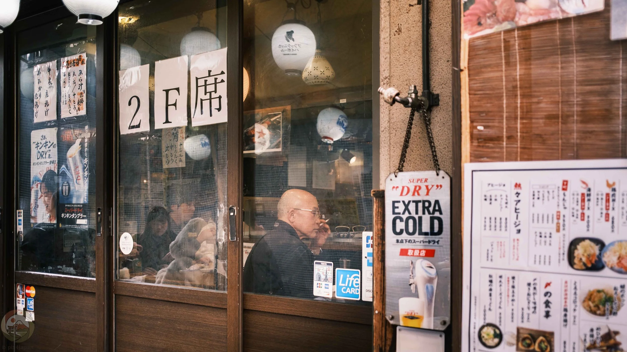 An elderly man relaxing at an izakaya beneath elevated train tracks in Tokyo’s Ameya-Yokocho (Ameyoko) district.