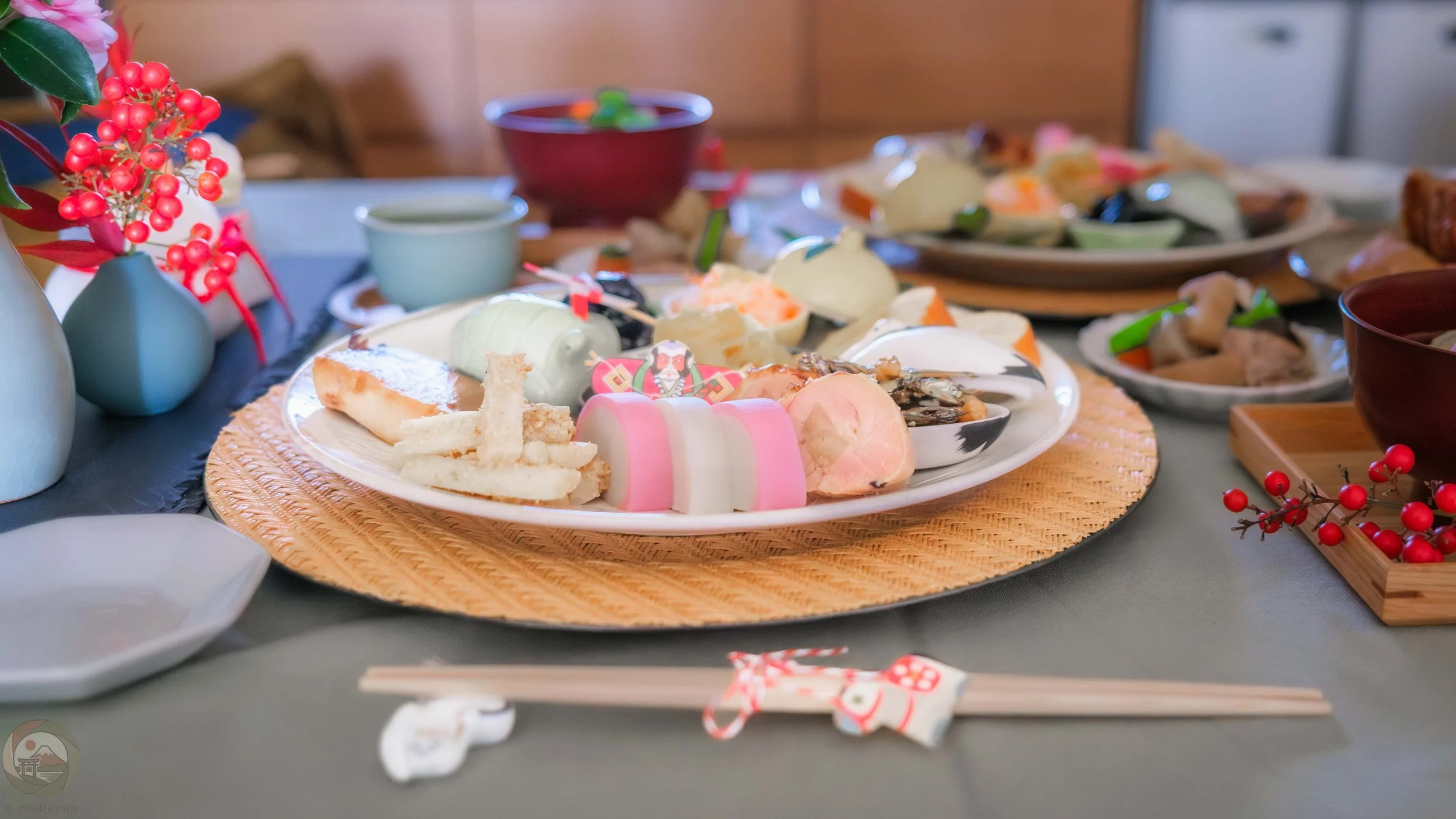 view of a traditional Japanese New Year’s Day osechi ryori meal with assorted dishes, soup, chopsticks, and tea arranged on a table.