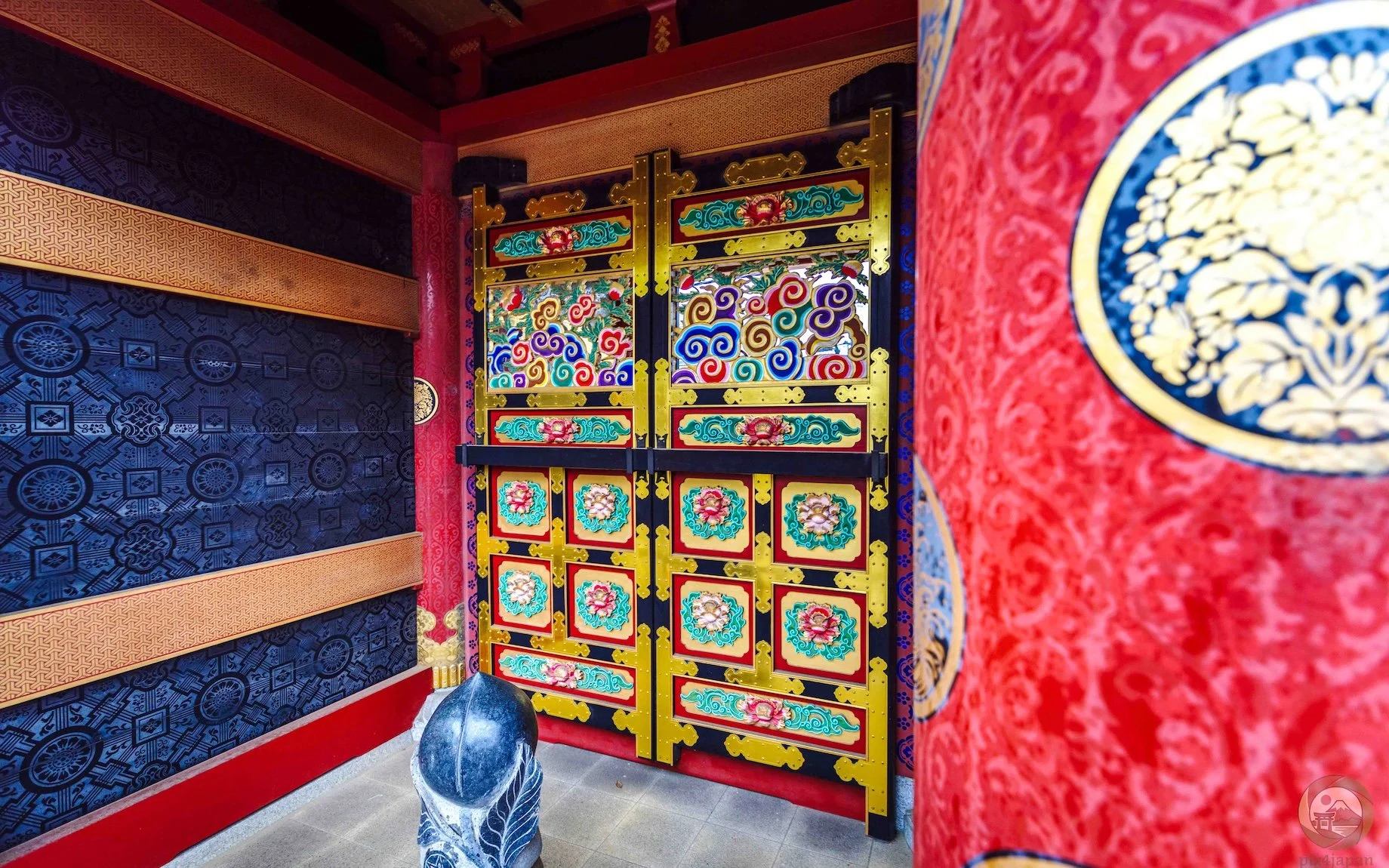 Ornate doorway of the Kirin-mon Gate at Osugi Shrine in Ibaraki, Japan, featuring red, indigo, green, and gold decorative woodwork with intricate floral and cloud motifs.