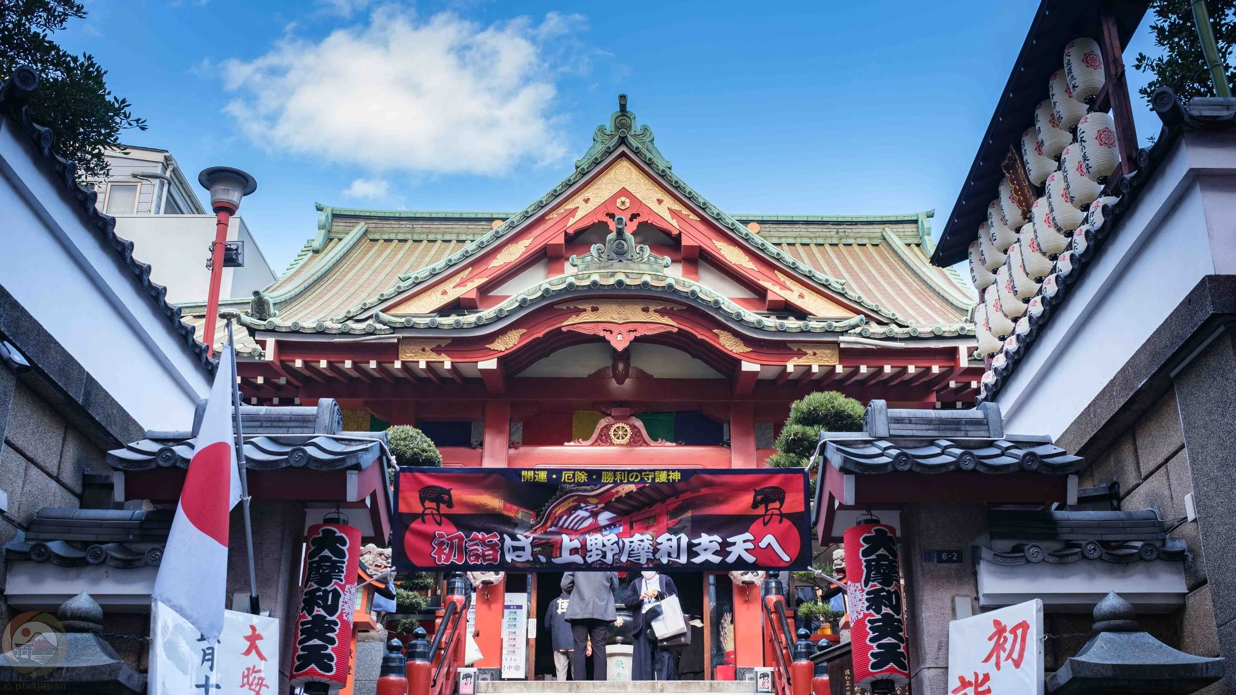 Visitors ascend and descend the stone steps of Marishiten Tokudai-ji, a Buddhist temple in Ueno, Tokyo, during the New Year season, framed by red railings, vertical banners, and hanging paper lanterns.