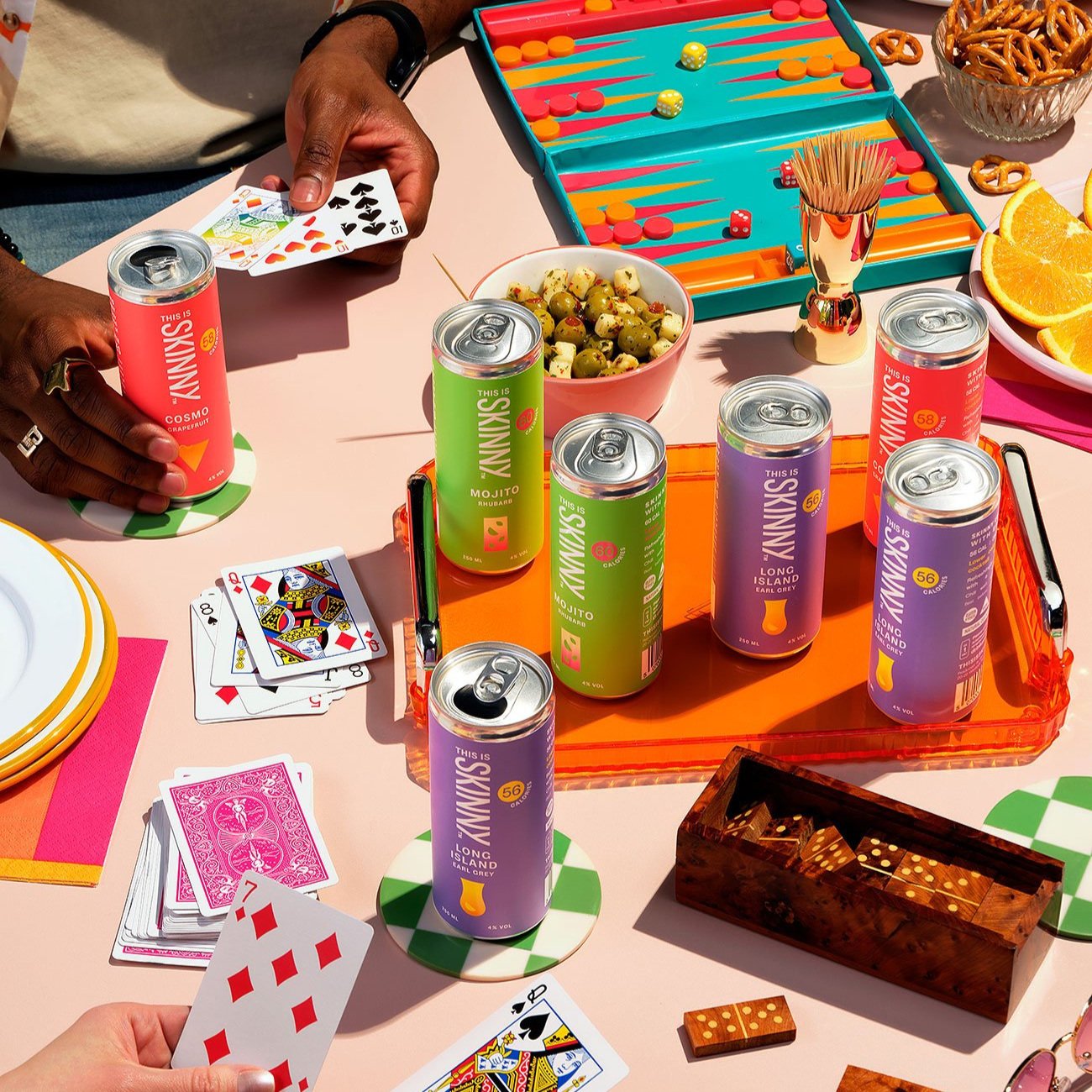 The table filled with board games, snacks and multiple This Is Skinny cocktail cans.