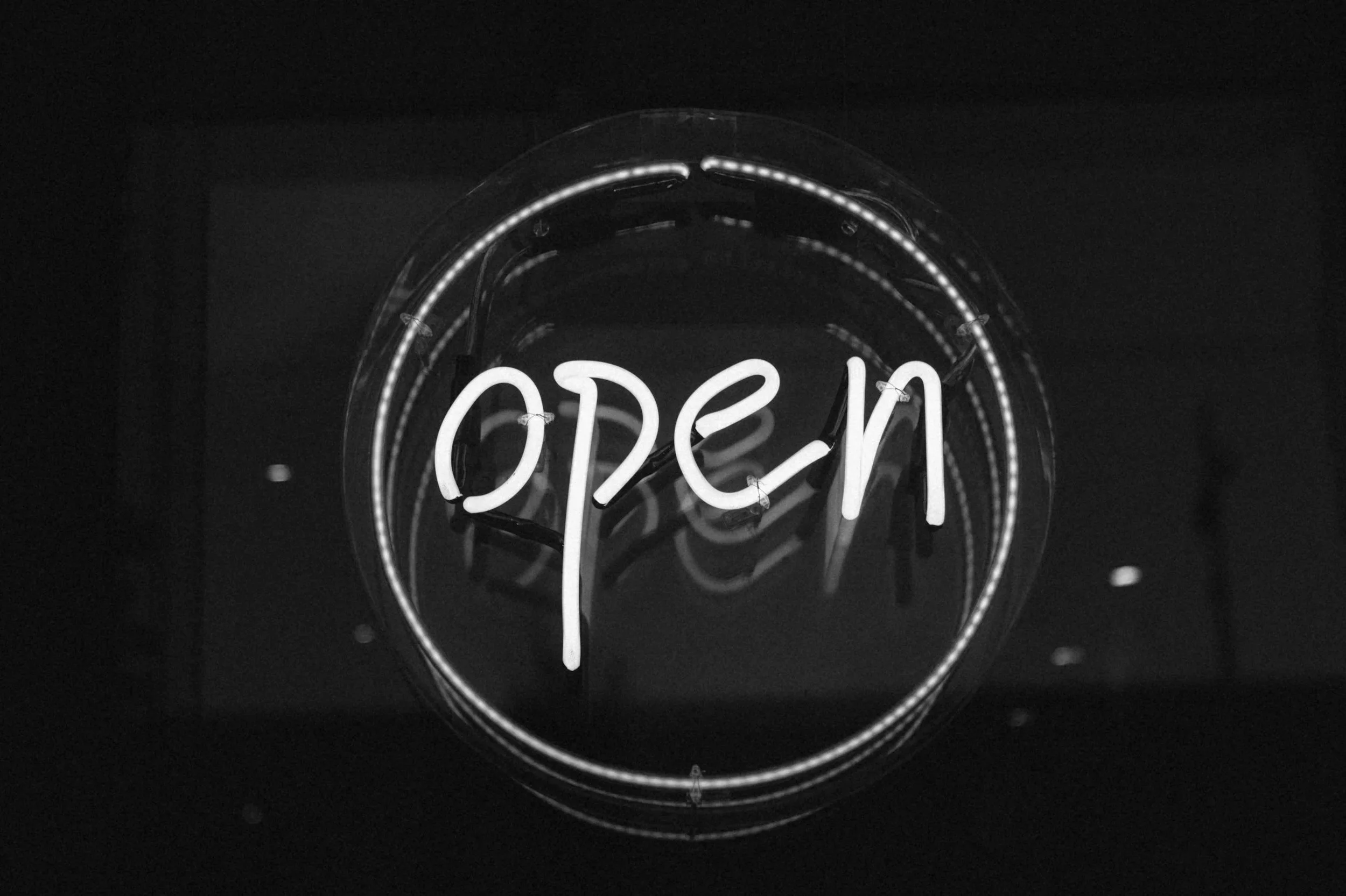 Neon sign that says 'Open' in cursive, glowing white against a dark background.