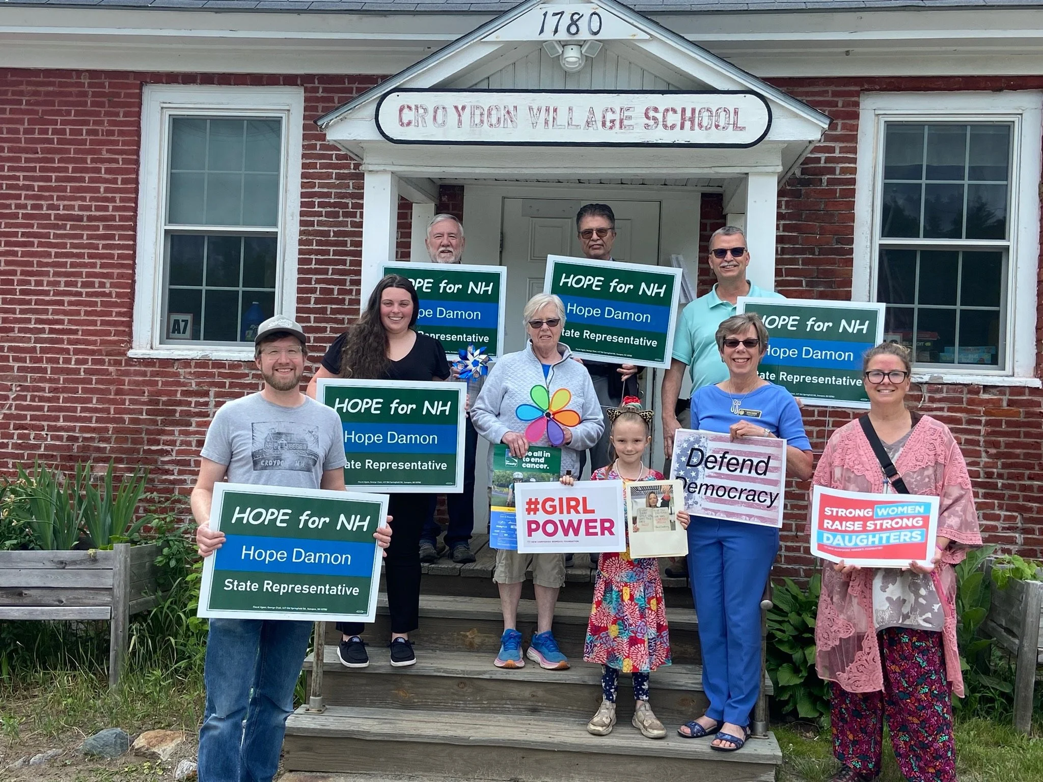 Hope and several volunteers hold Hope for NH signs on the steps of the Croydon Village School