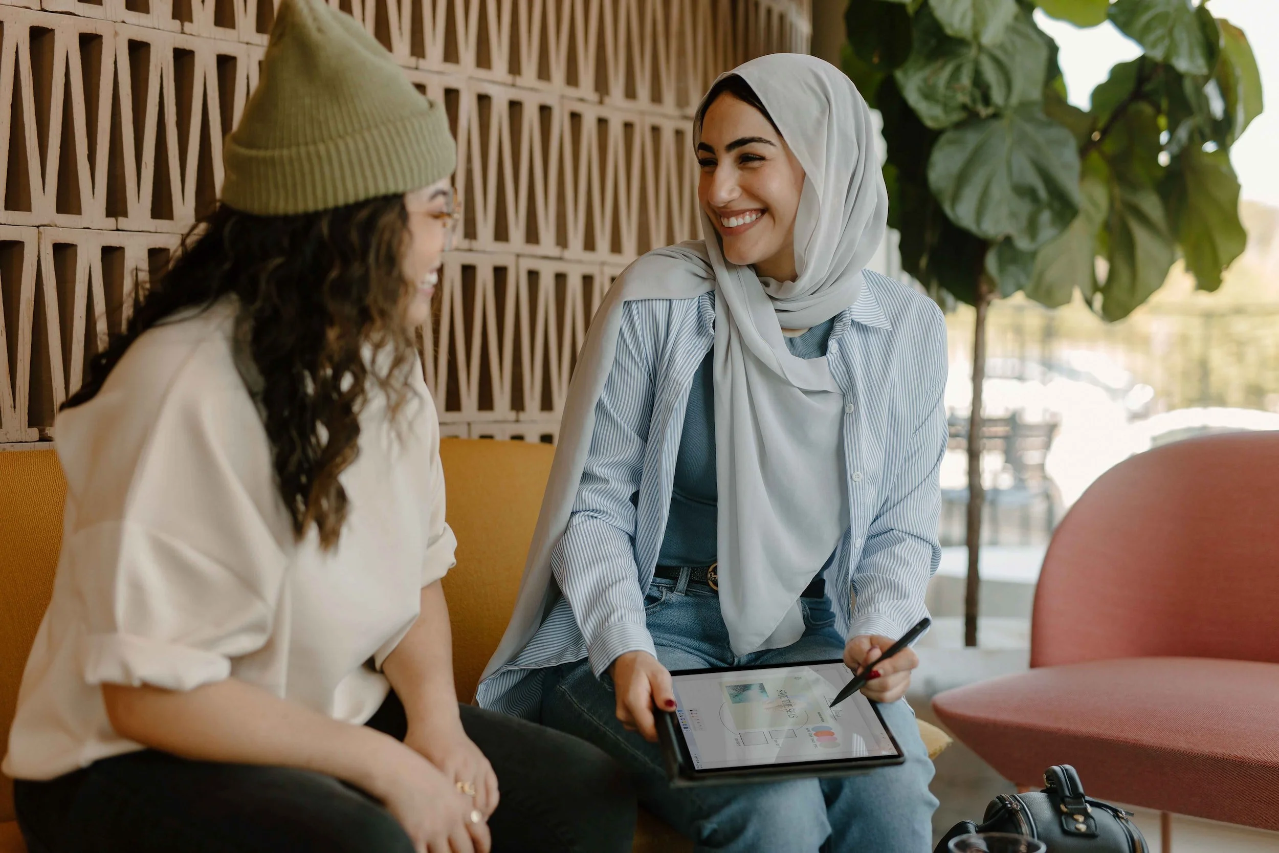 Two people sitting down and smiling. One person is holding a tablet with charts and tables on the screen.